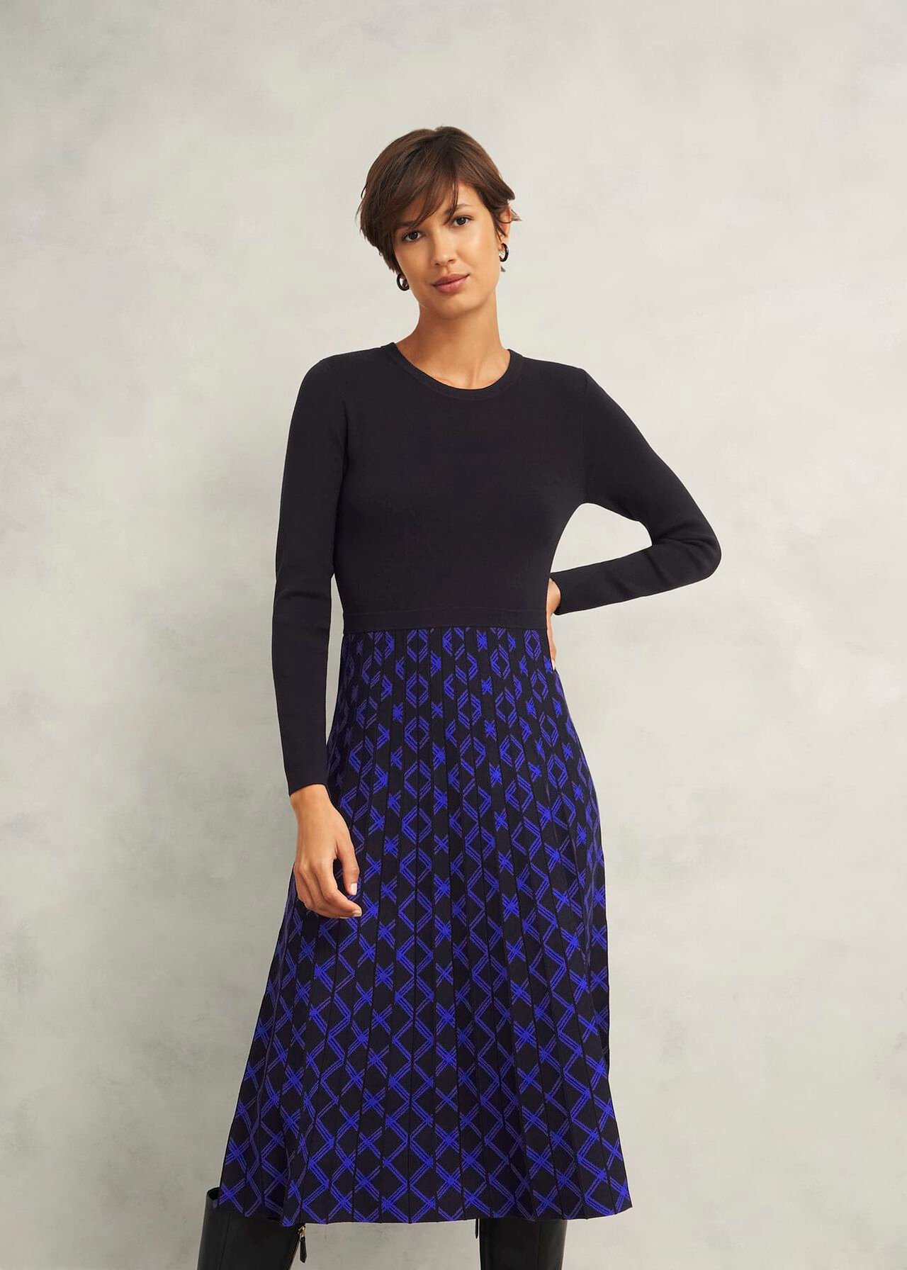 A woman wearing a black long-sleeve dress with a blue geometric patterned skirt, standing against a plain background.