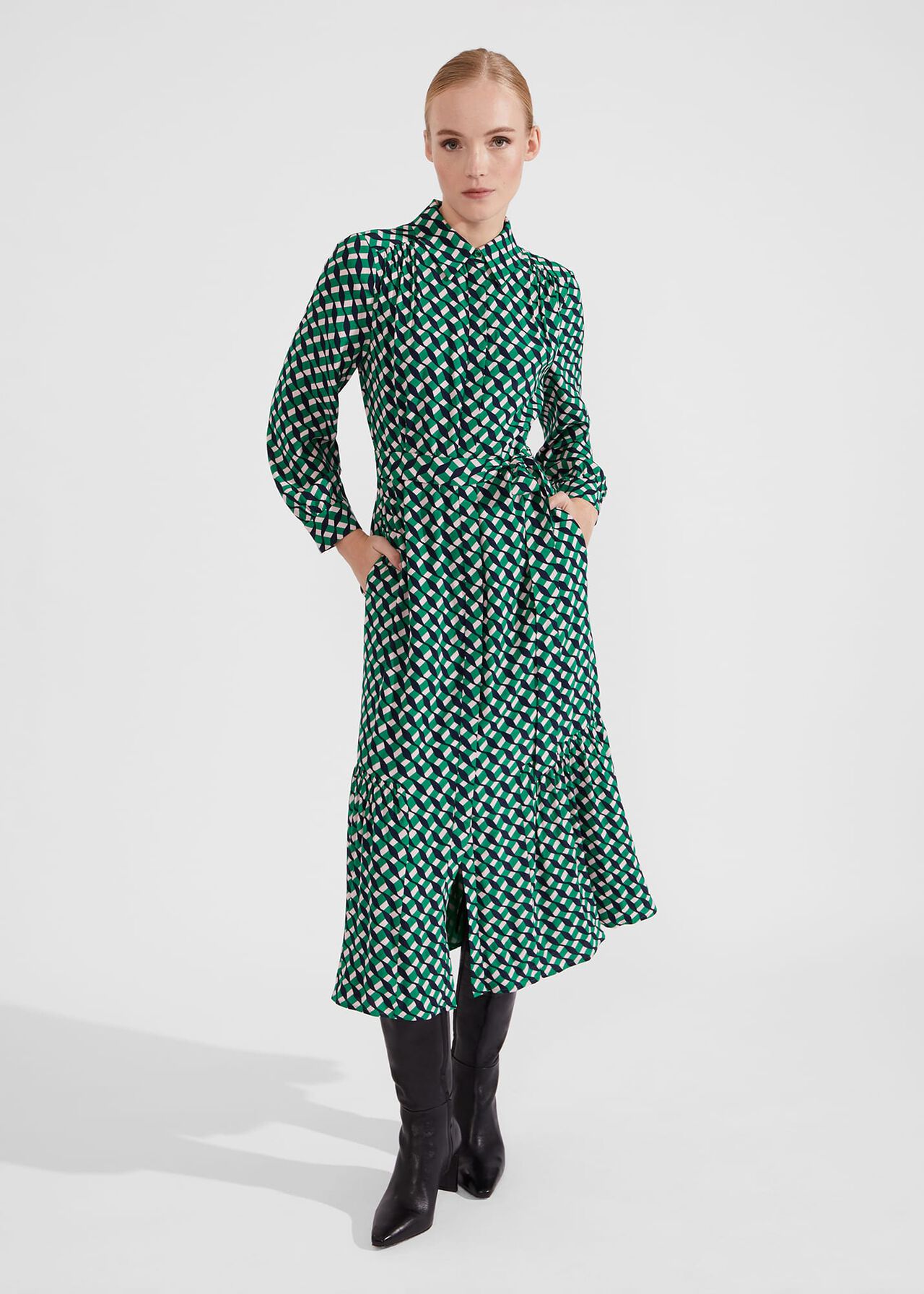 A woman wearing a midi dress with a geometric pattern in green, black, and white, featuring a collar, long sleeves, and front fastening.