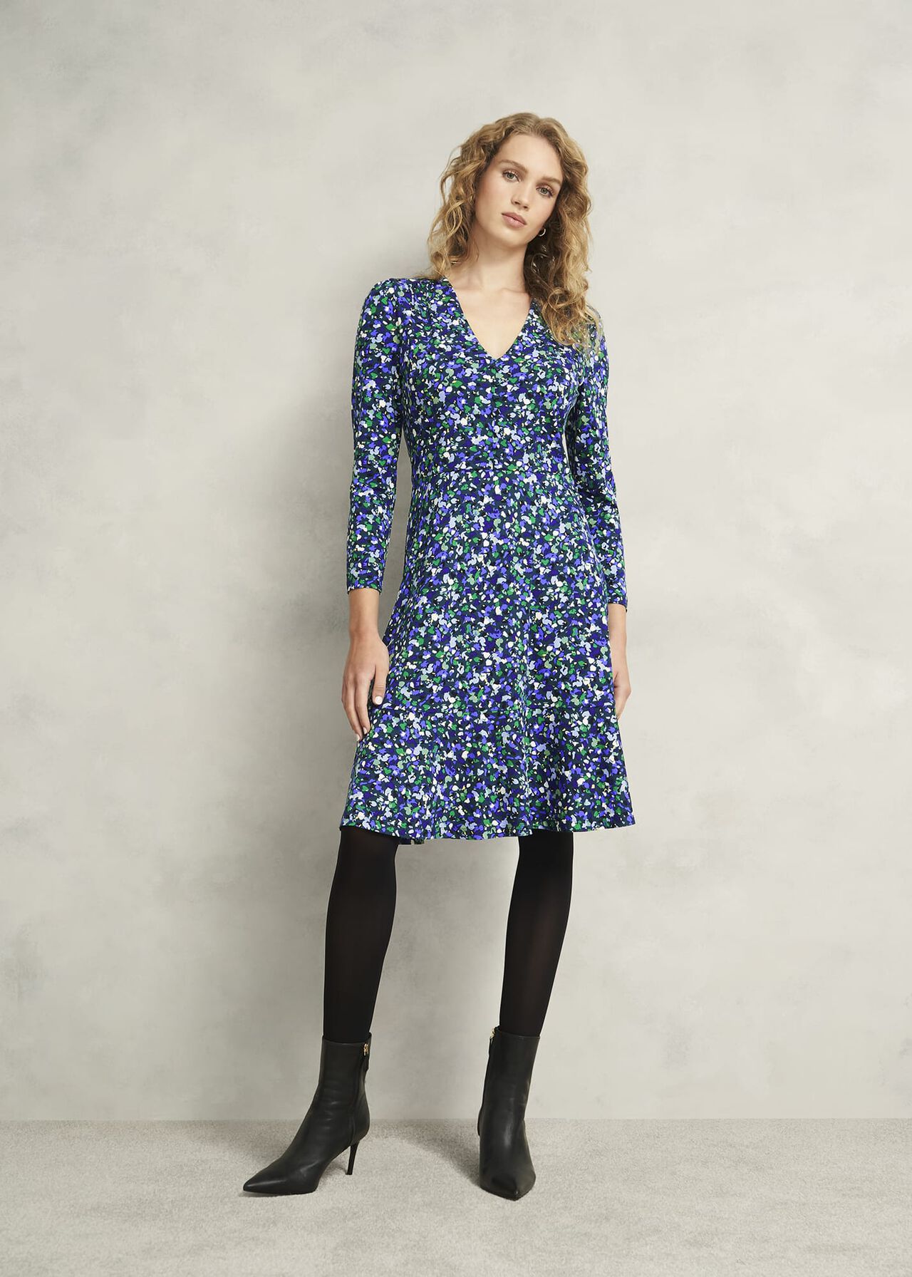 A woman wearing a blue floral jersey dress with long sleeves and a V-neckline, standing against a plain background.
