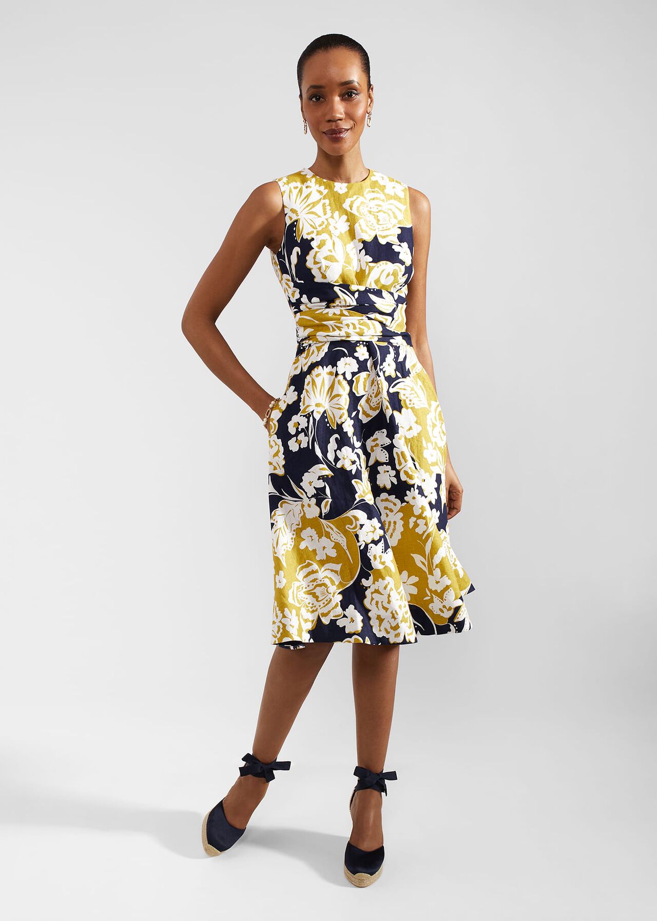 A woman wearing a sleeveless navy blue linen dress with a yellow and white floral pattern, crew neckline, and knee-length hem.