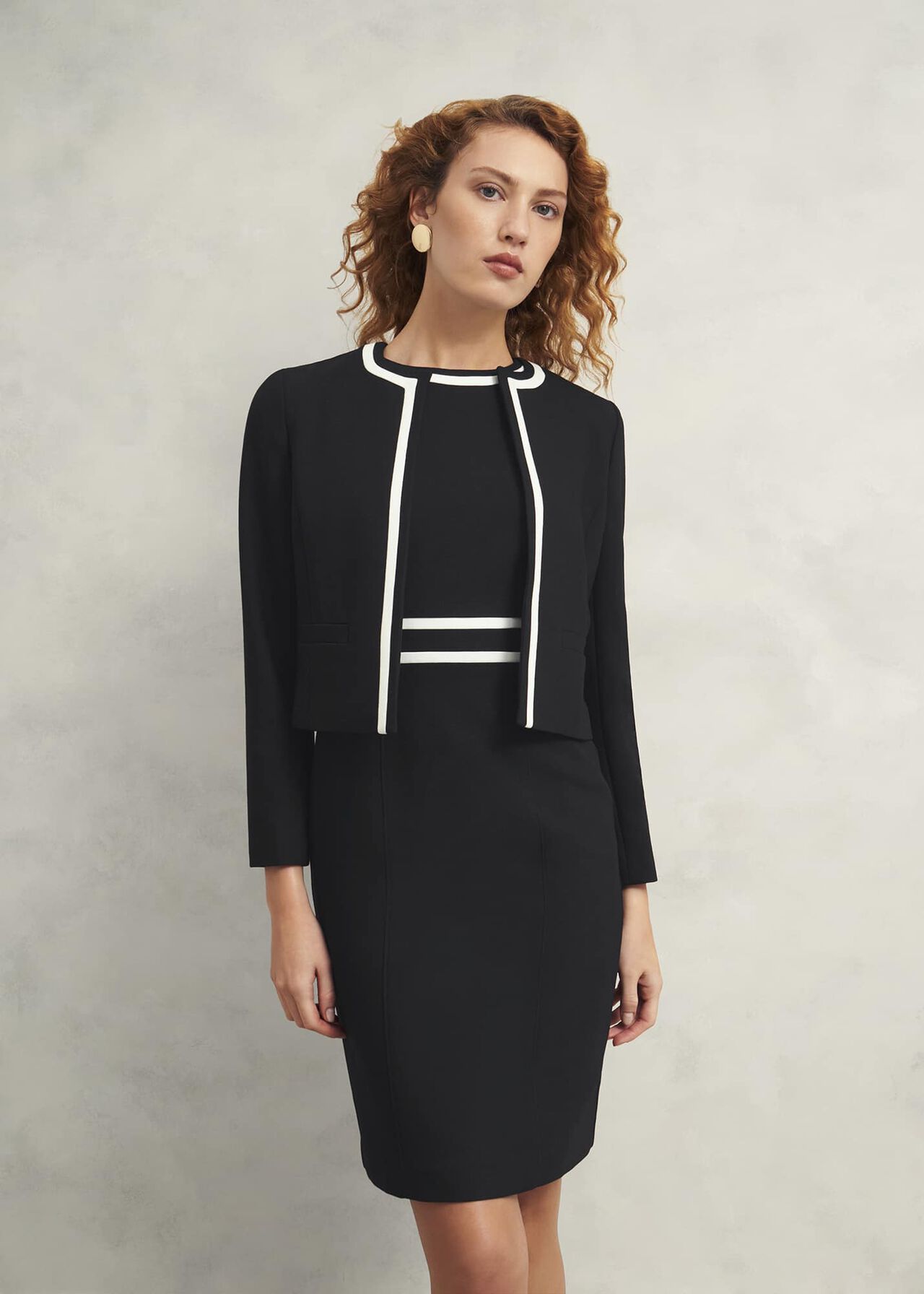 A woman wearing a black, collarless, tailored women's jacket with long sleeves, made from a fabric blend, with a smooth lining, standing against a neutral background.