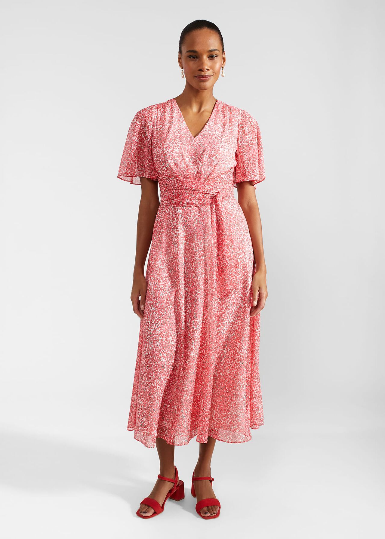 A woman wearing a pink and white floral wrap dress with short flutter sleeves, V-neckline, waist tie, and a back zip fastening.