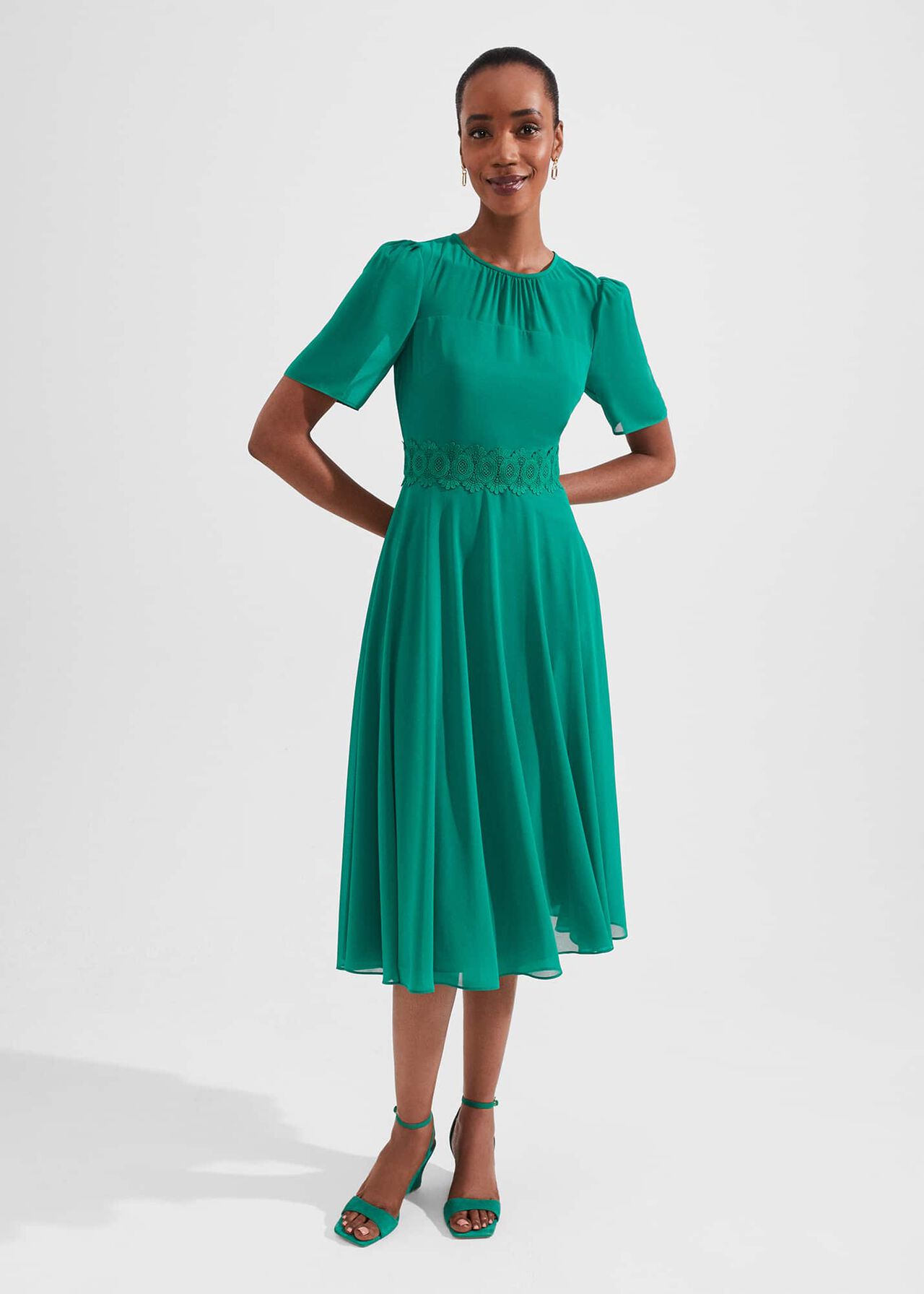 A woman wearing a teal green midi dress with short puffed sleeves, a crew neckline, lace detail at the waist, and a flowing skirt.