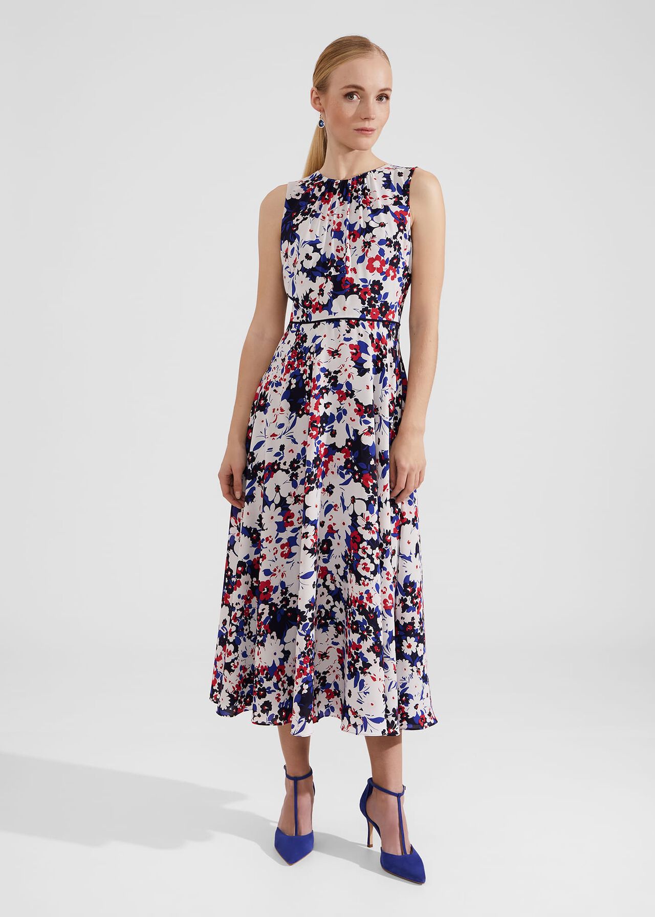A woman wearing a sleeveless, midi-length floral dress with a gathered crew neckline, featuring a multicolour floral pattern on a light background.