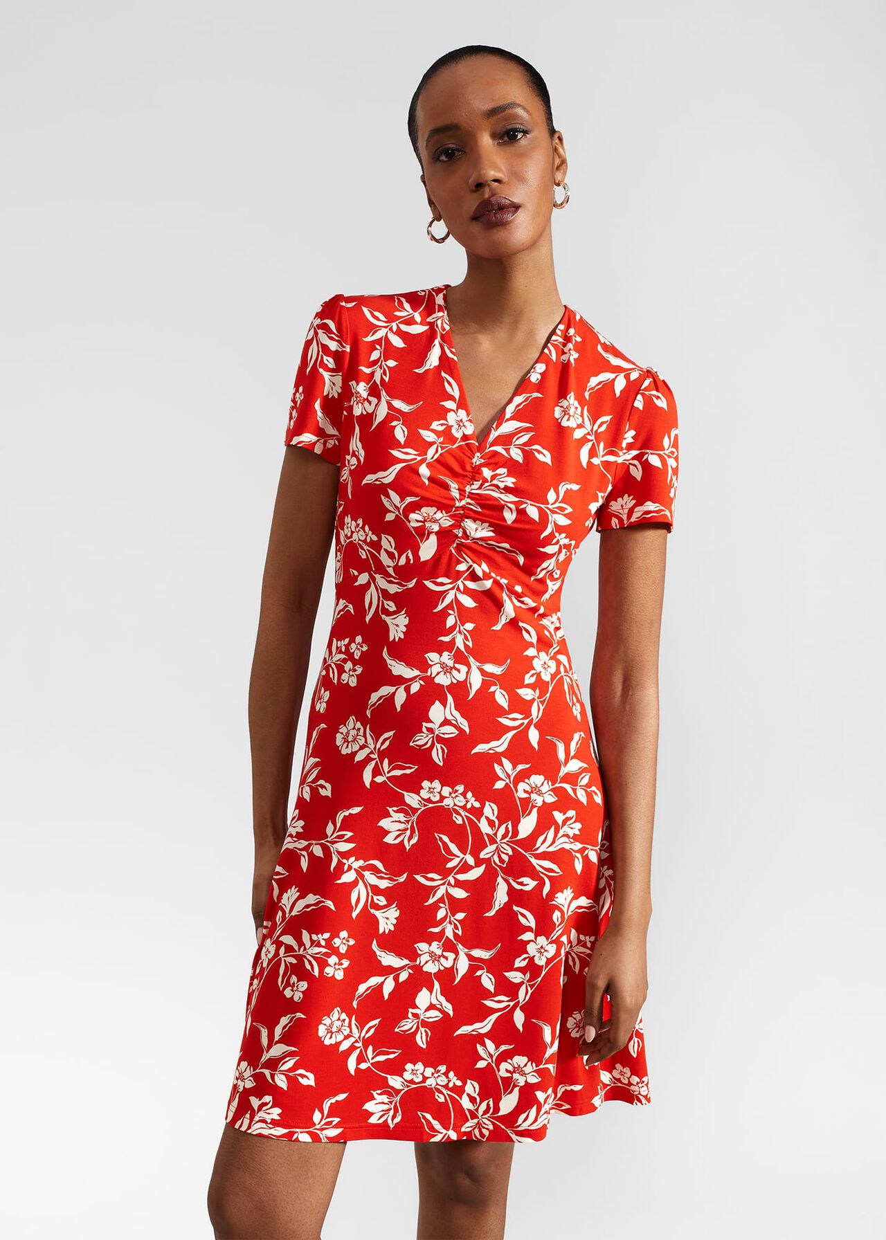 A woman wearing a red floral dress with a V-neckline and short sleeves, standing against a plain background.