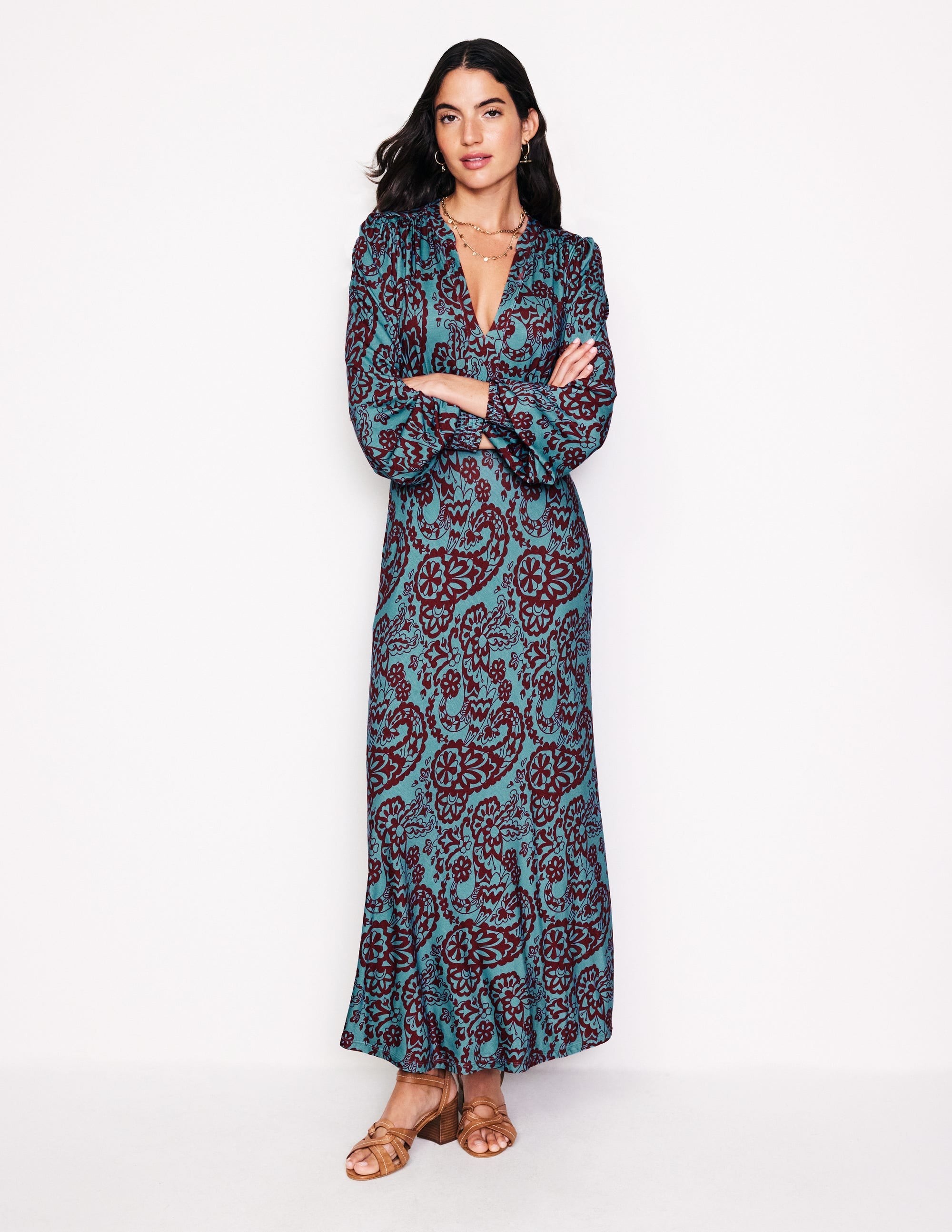 A woman wearing a blue and burgundy paisley patterned midi dress with a smocked waist and notch neckline.