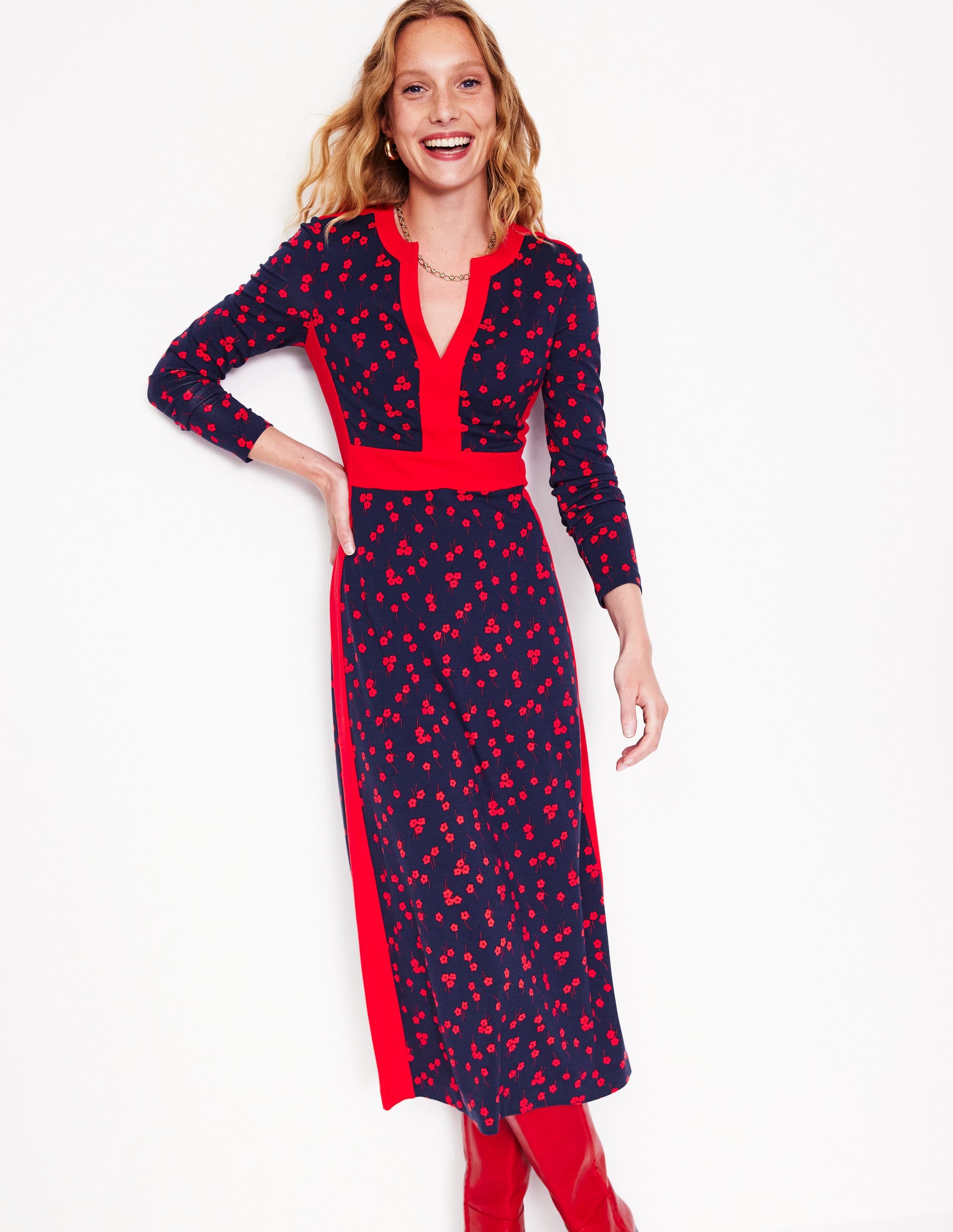 A woman wearing a red midi dress with a floral pattern, long sleeves, and a fitted waist, standing against a white background.