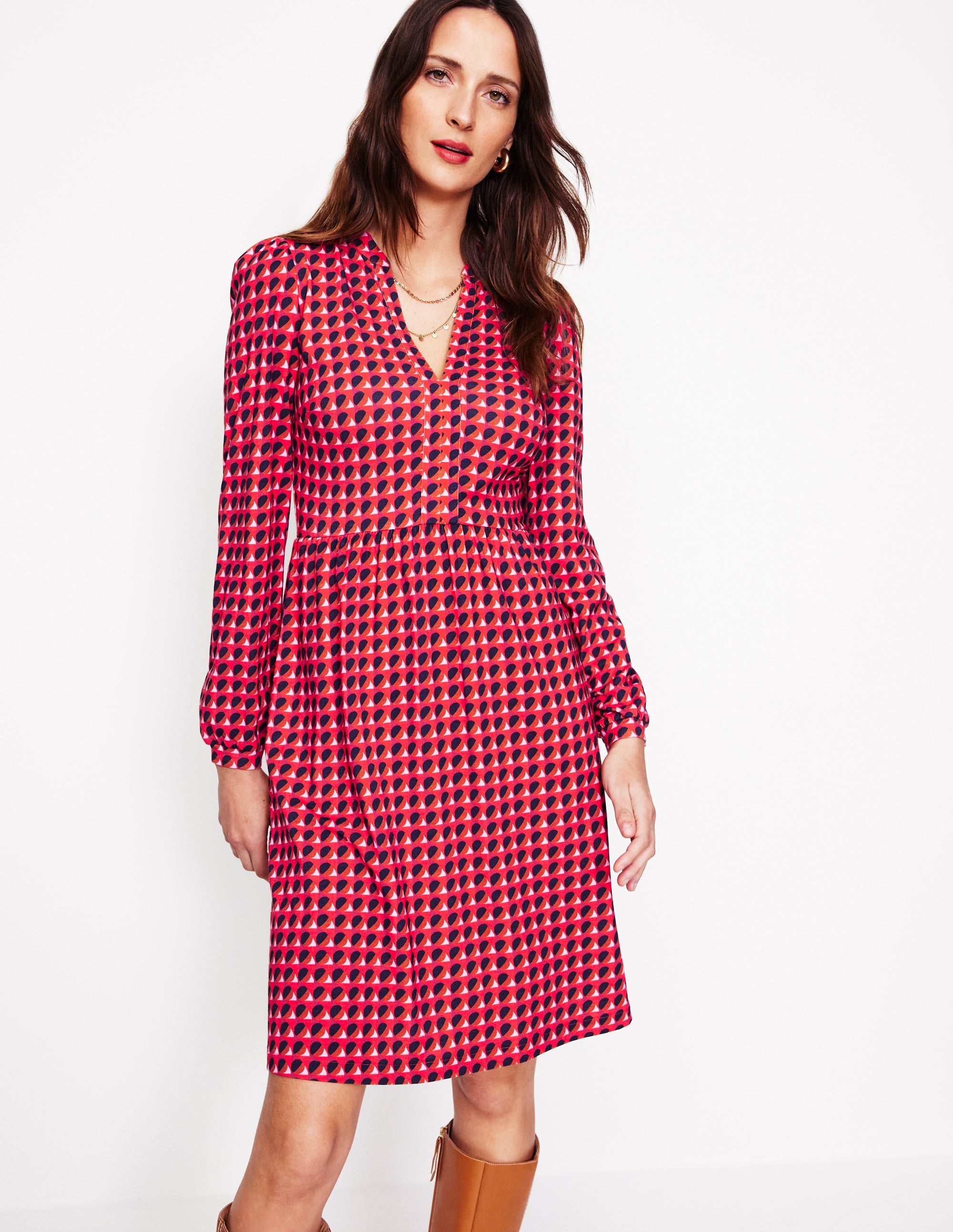 A woman wearing a red jersey dress with a sphere geo print pattern, long sleeves, V-neckline, and knee length.