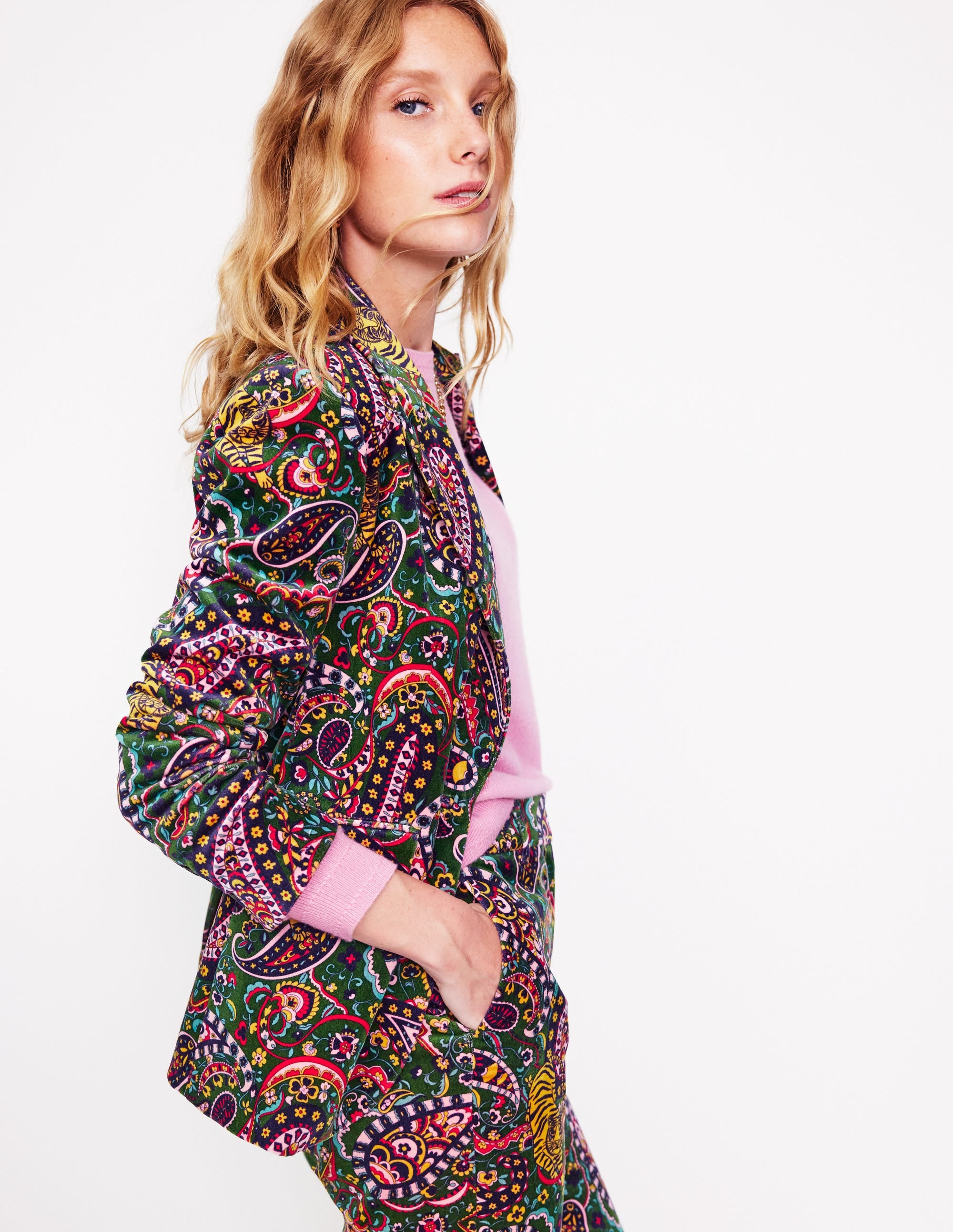 A woman wearing a vibrant, multicolour velvet blazer with a Tiger Bloom pattern, featuring a revere collar, contrast piping, and welt pockets.