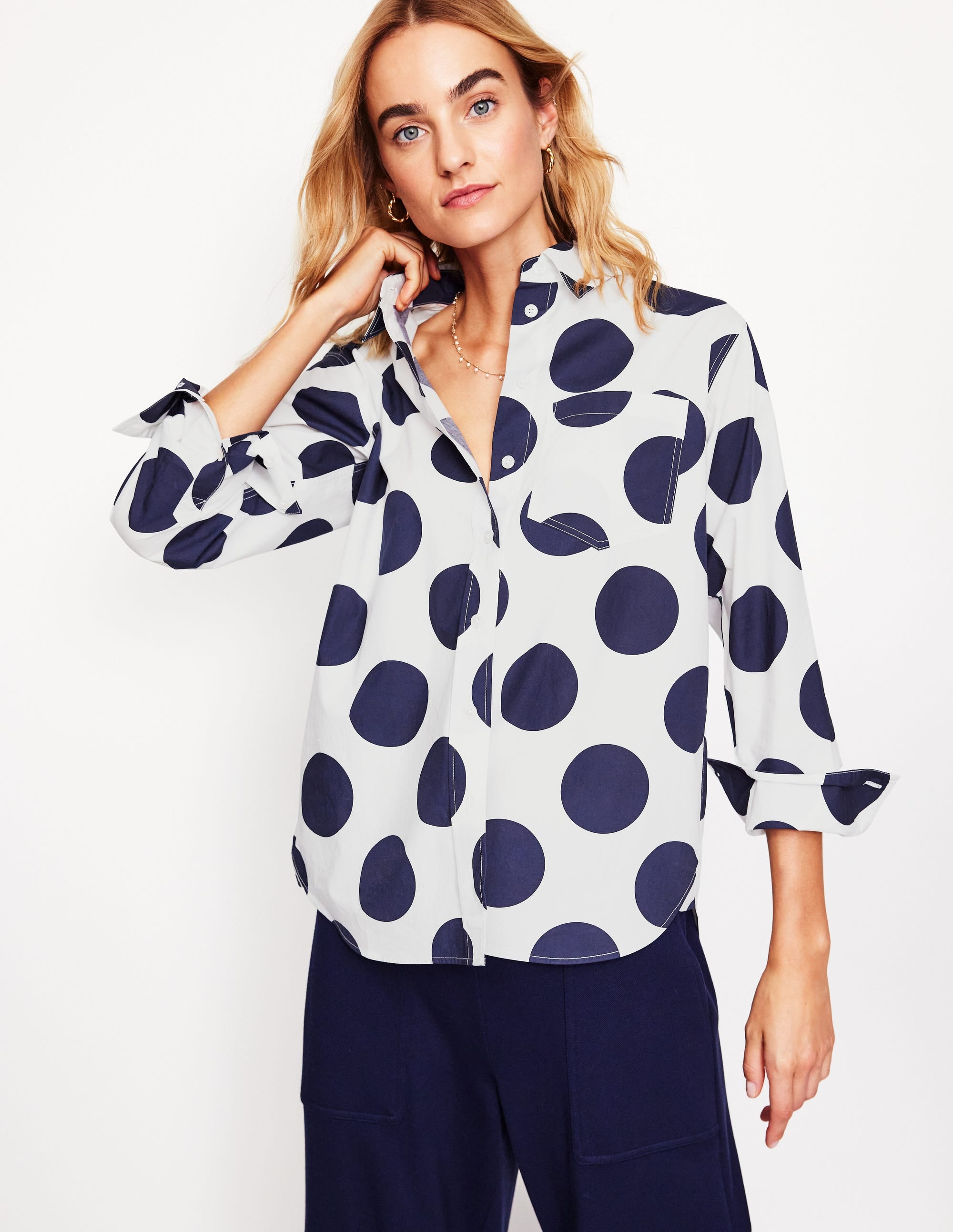A woman wearing a white cotton shirt with navy blue orderly spots, a classic collar, and a curved hem, styled casually.