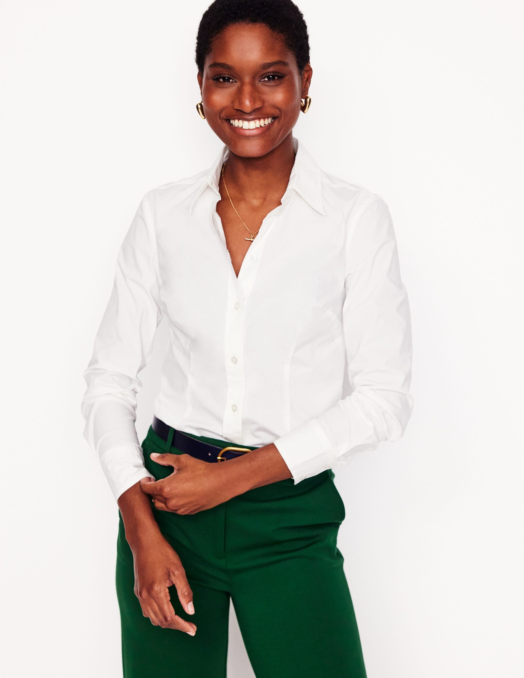 A woman wearing a white fitted cotton shirt with a classic collar and long sleeves, smiling against a plain background.