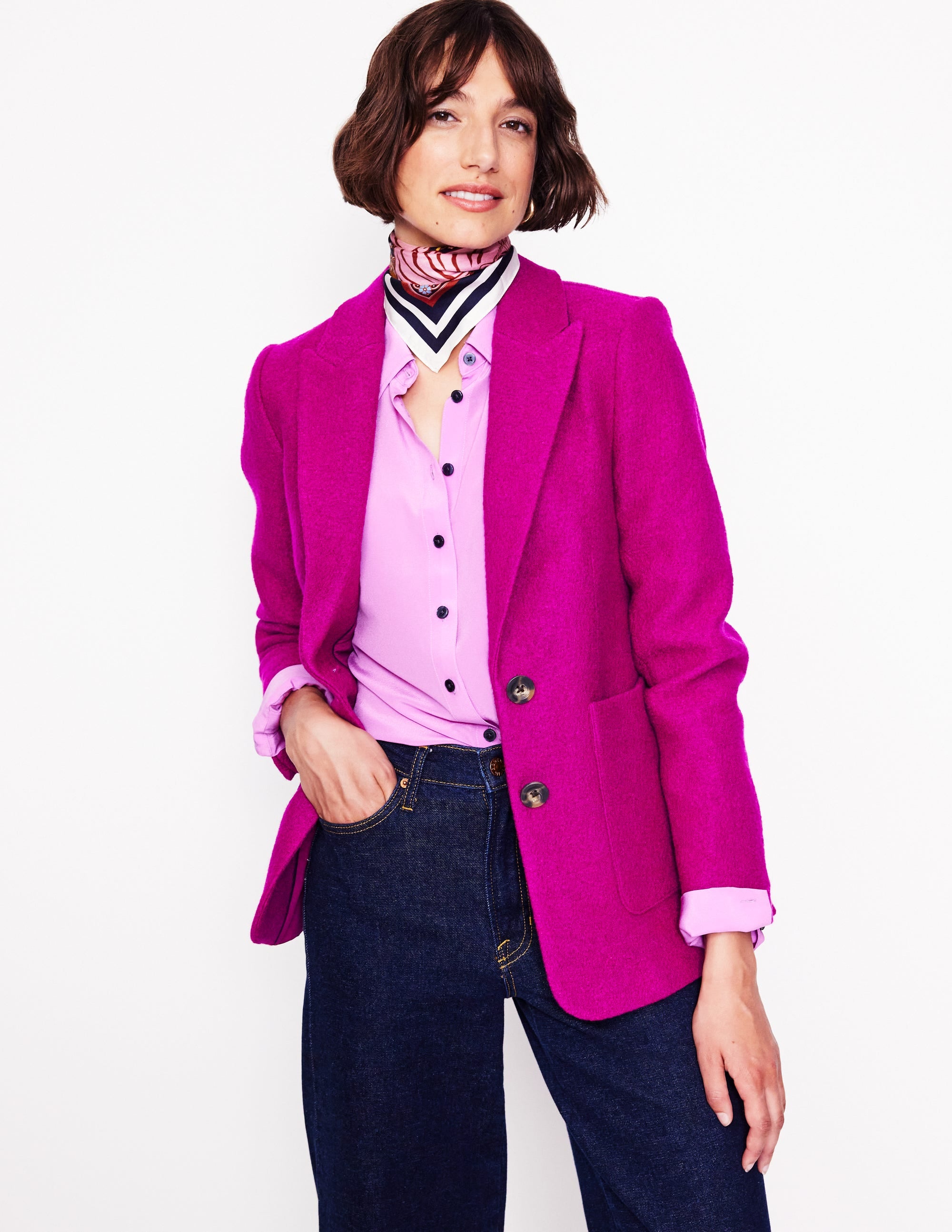 A woman wearing a vibrant plum textured blazer with a revere collar, contrast piping, and welt pockets.