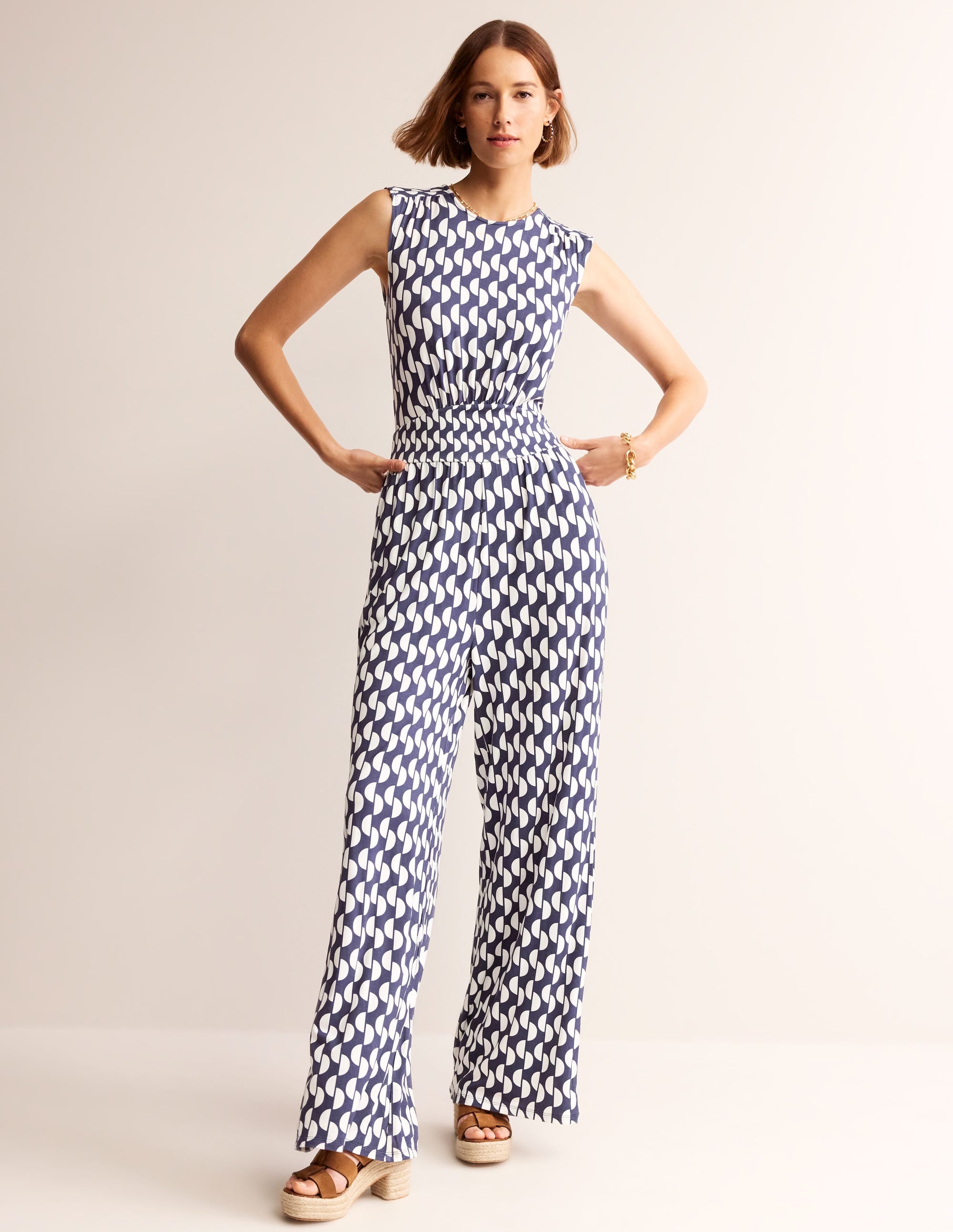 A woman wearing a navy blue jumpsuit with a white geometric wave pattern, sleeveless design, and a fitted silhouette.