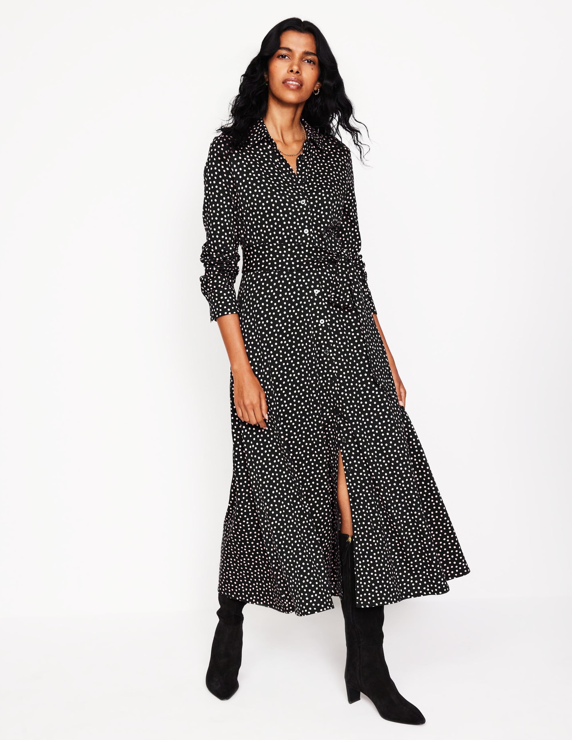 A woman wearing a black midi shirt dress with white abstract dots, long sleeves, and a waist belt, paired with black boots.