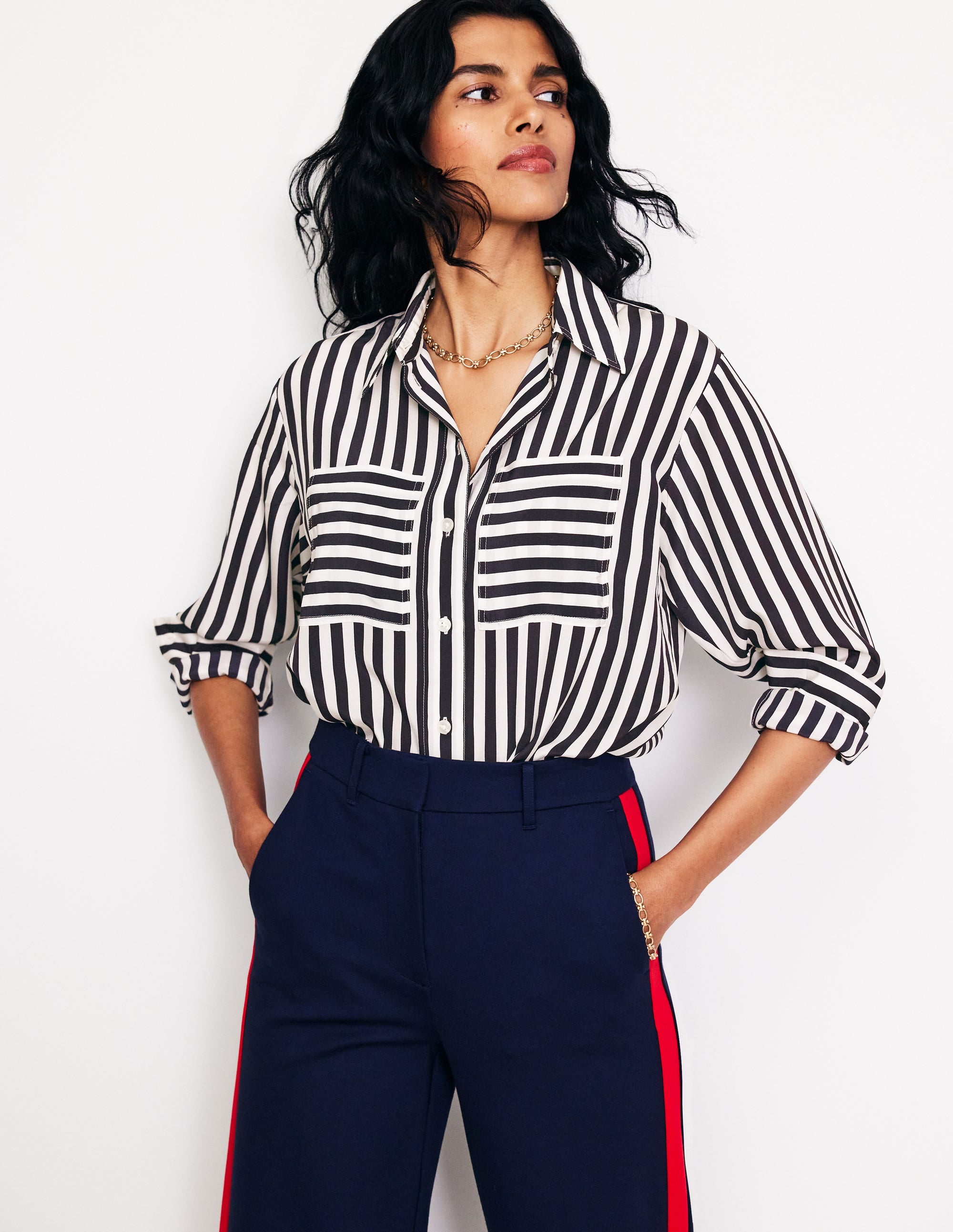 A woman wearing a navy and white striped silk shirt with a curved hem, button-down front, and long sleeves.