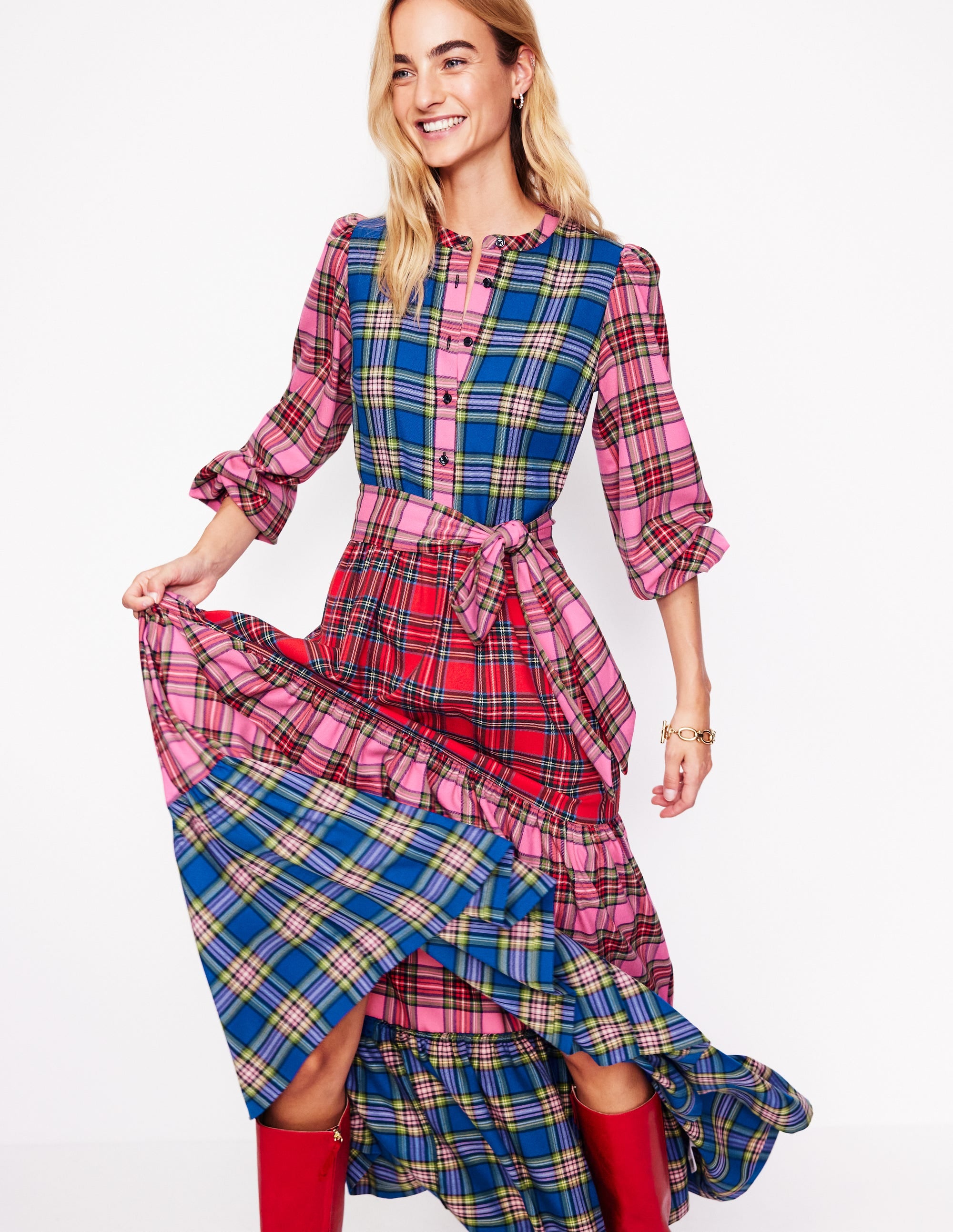 A woman wearing a multicolour hotch potch check maxi dress with a fitted bodice, flared skirt, side seam pockets, and a detachable belt.