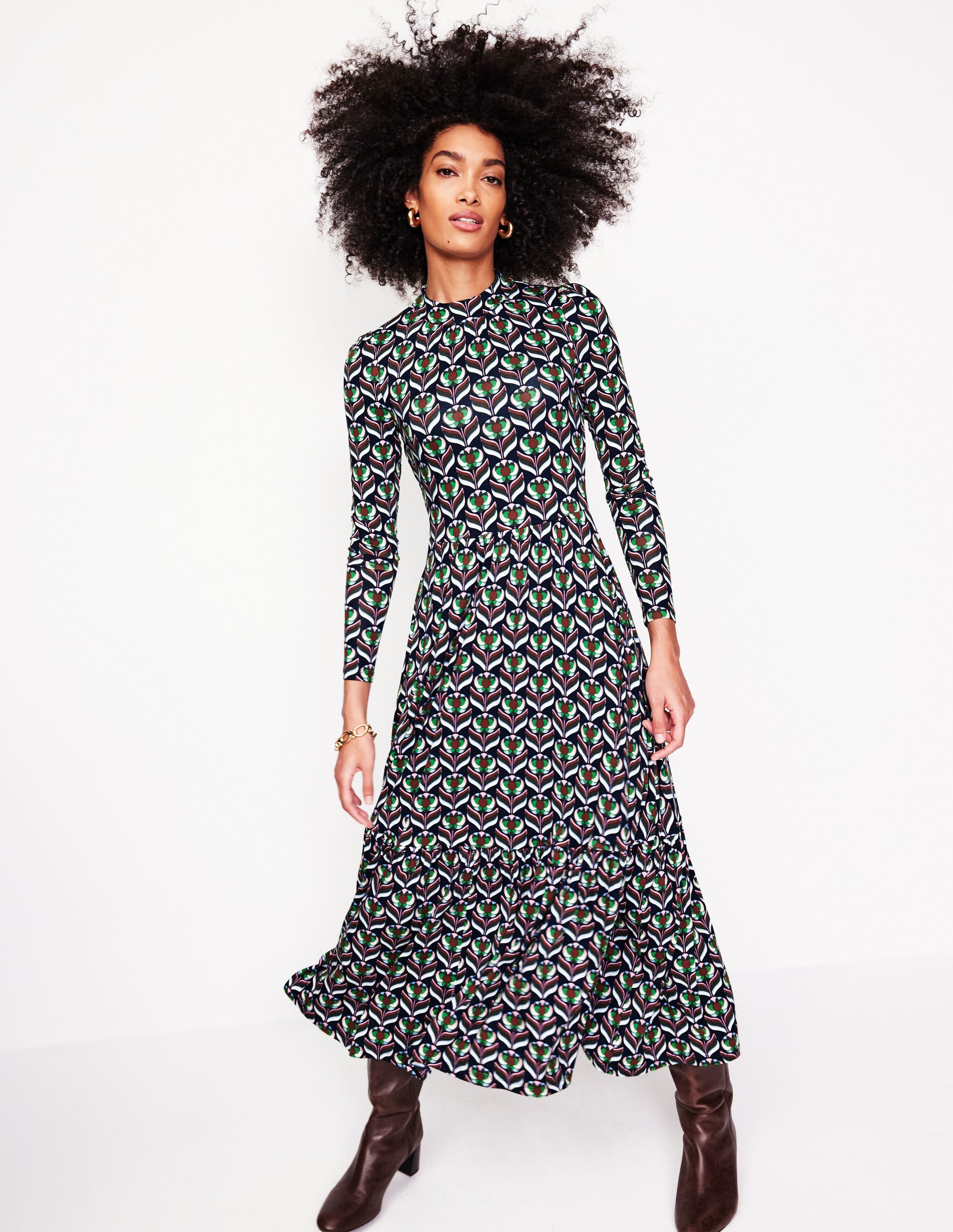 A woman wearing a navy high neck tiered jersey dress with a blossom stamp pattern, long sleeves, and a flowing, tiered skirt.