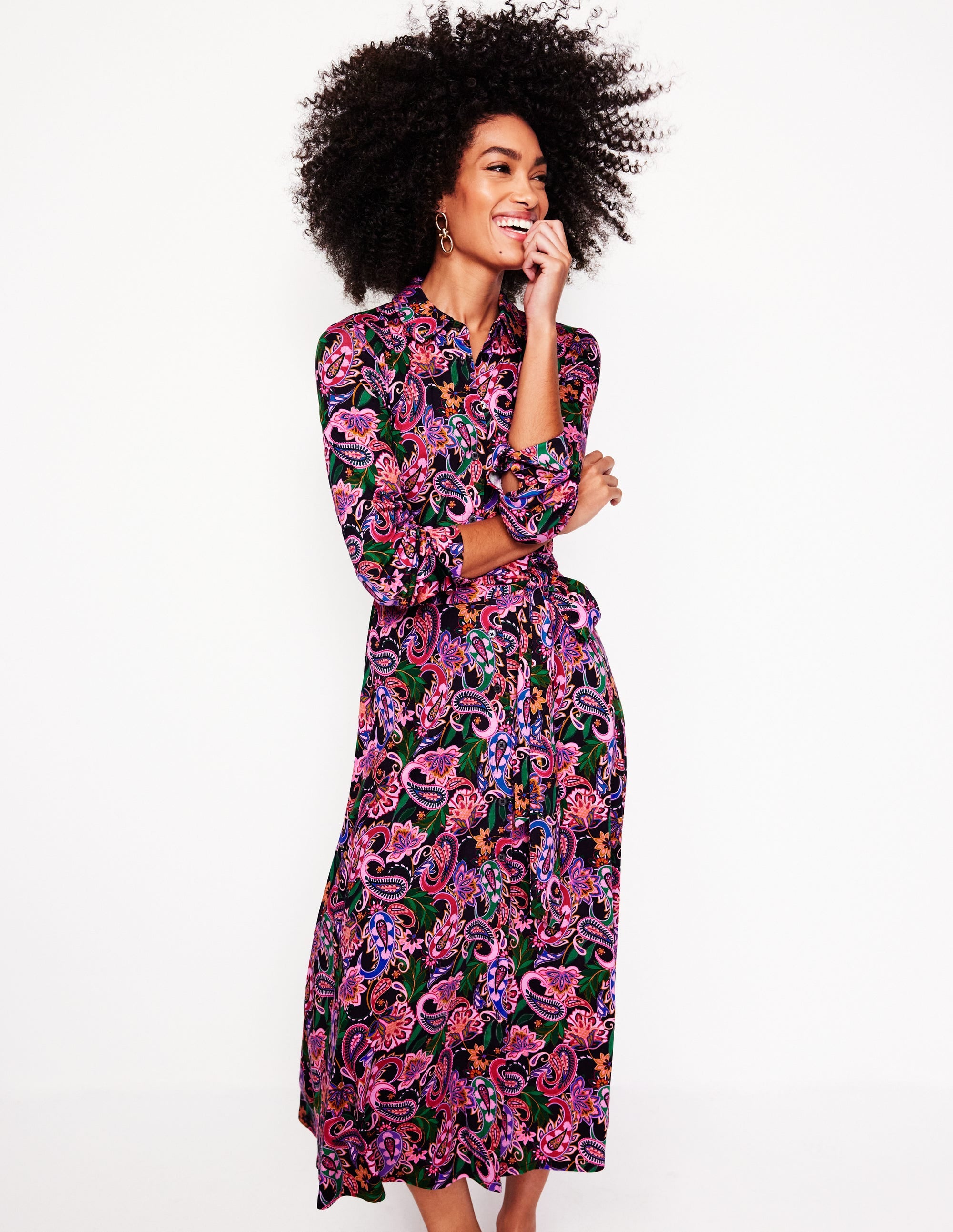 A woman wearing a colorful paisley print midi shirt dress with long sleeves, a collar, and a waist belt.