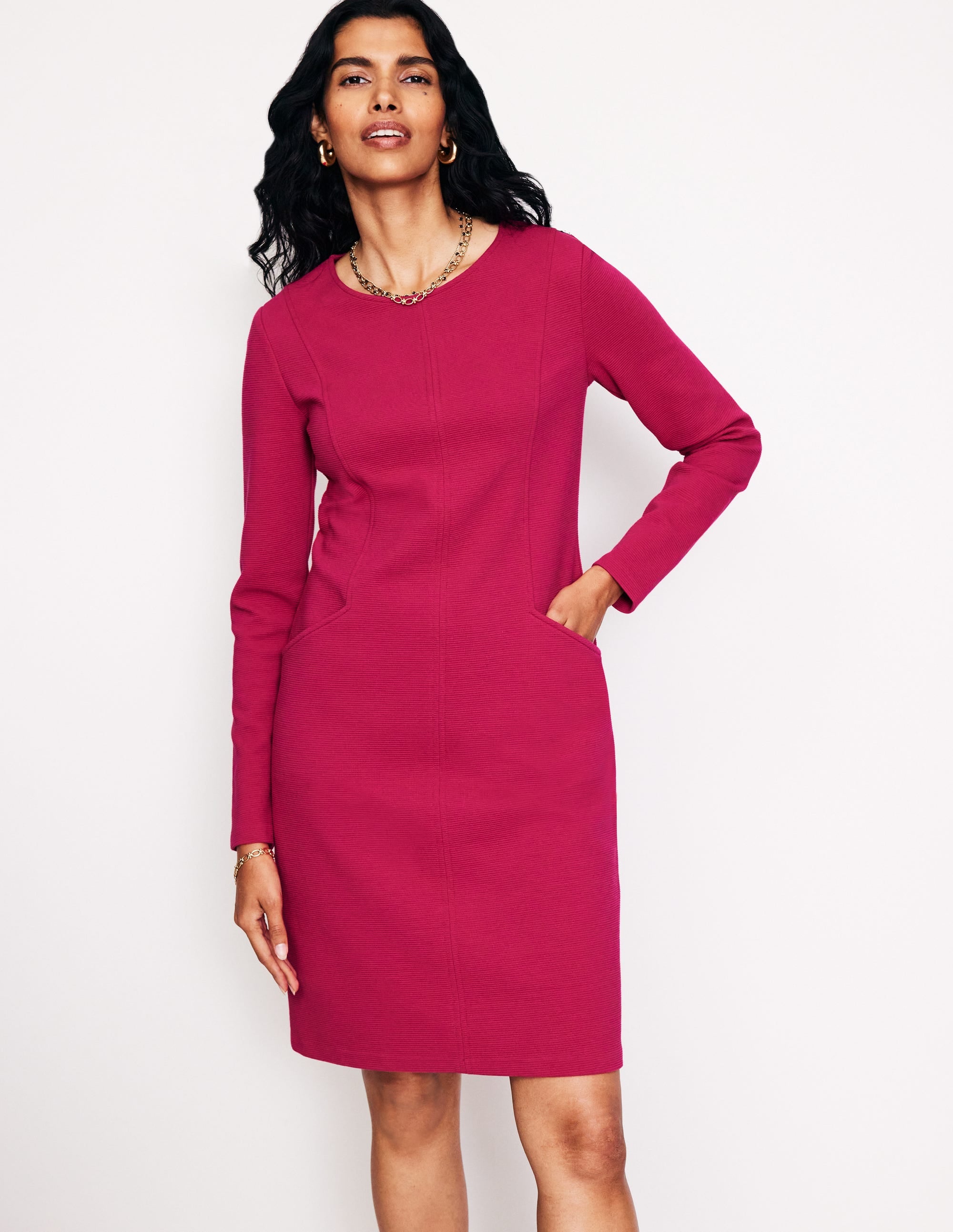 A woman wearing a cherry jam-colored Ottoman dress with three-quarter sleeves, front pockets, and above-the-knee length.