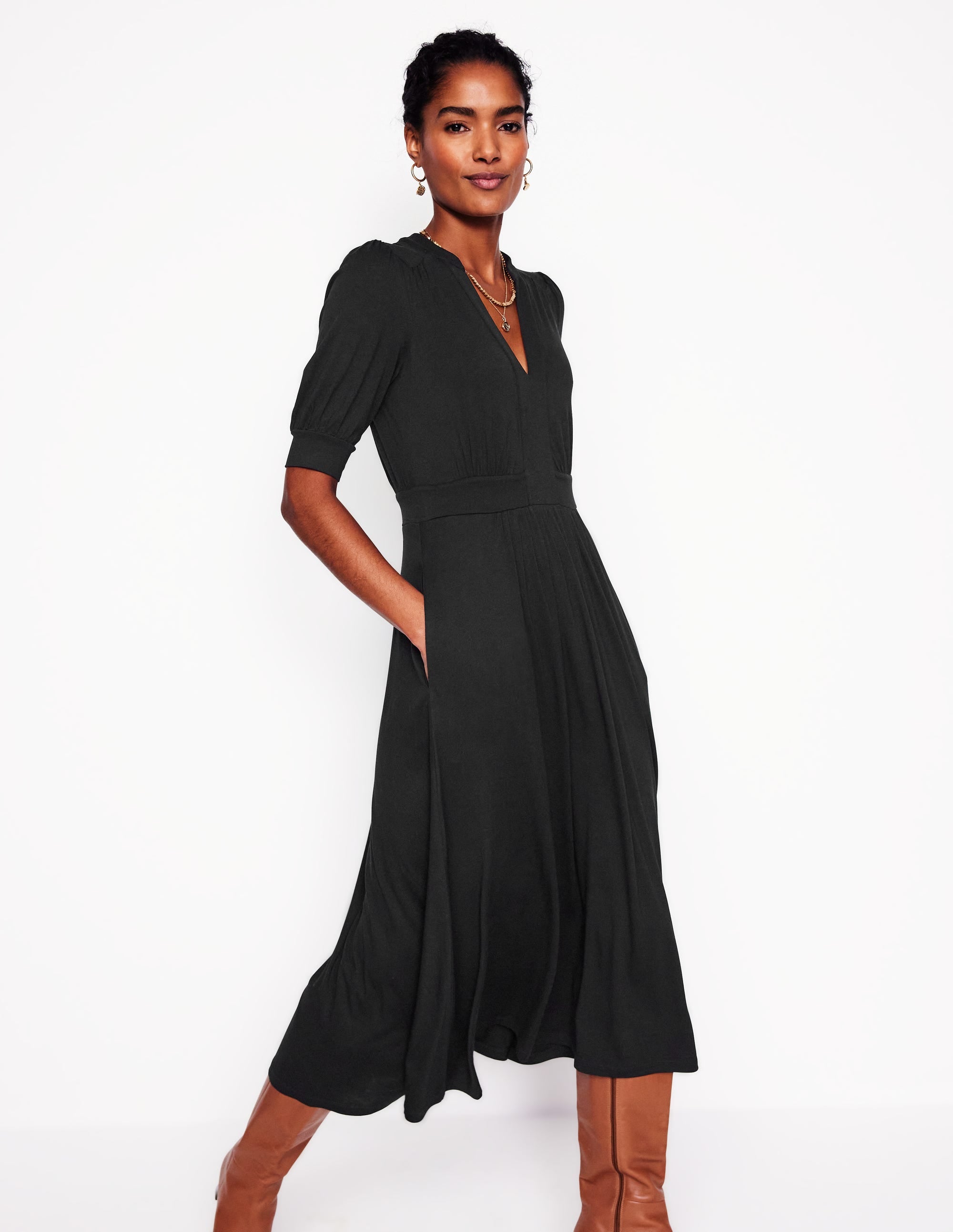 A woman wearing a black midi dress with puffed short sleeves, standing against a white background.