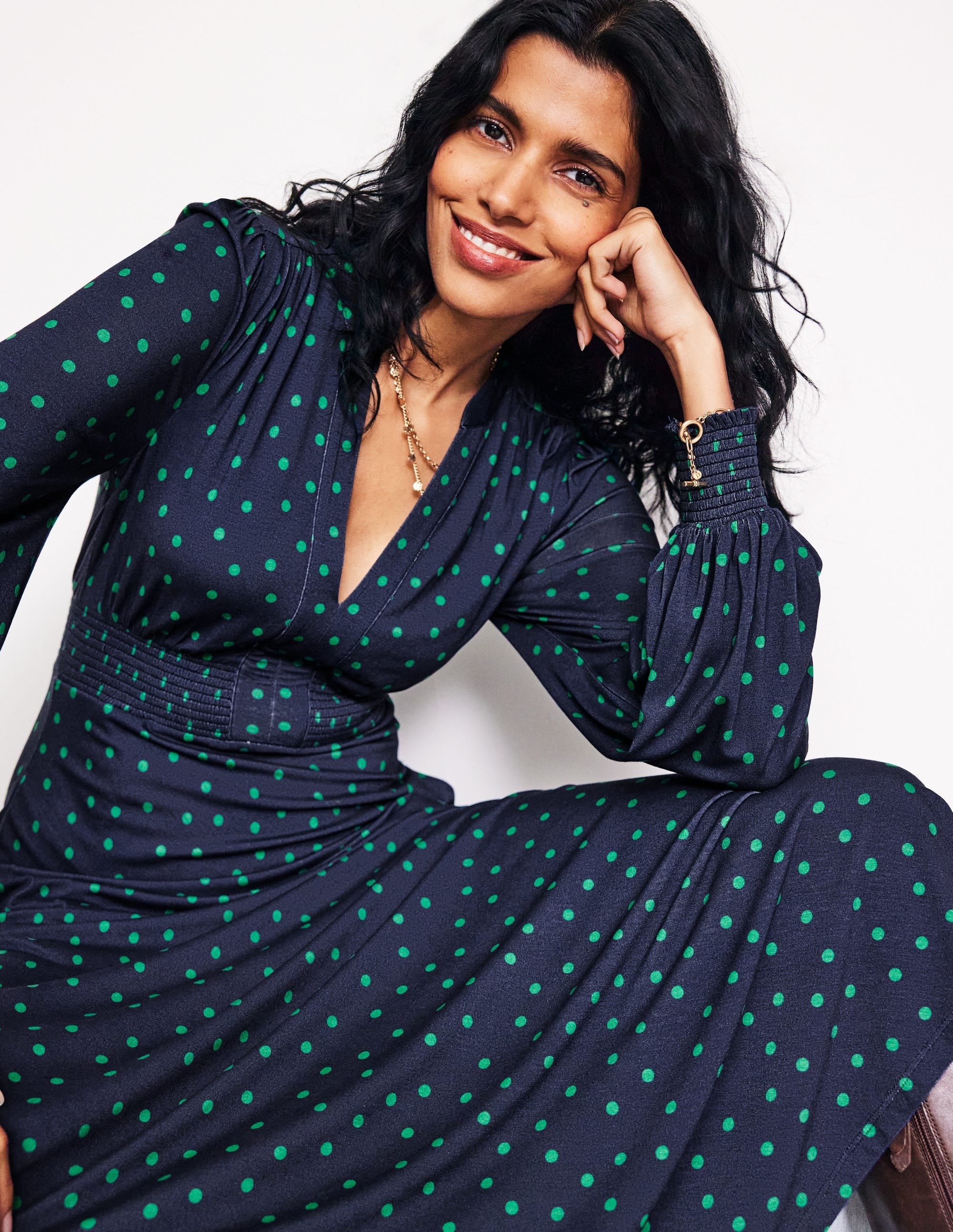 A woman wearing a navy midi dress with green sparse spots, featuring a smocked waist and notch neckline.
