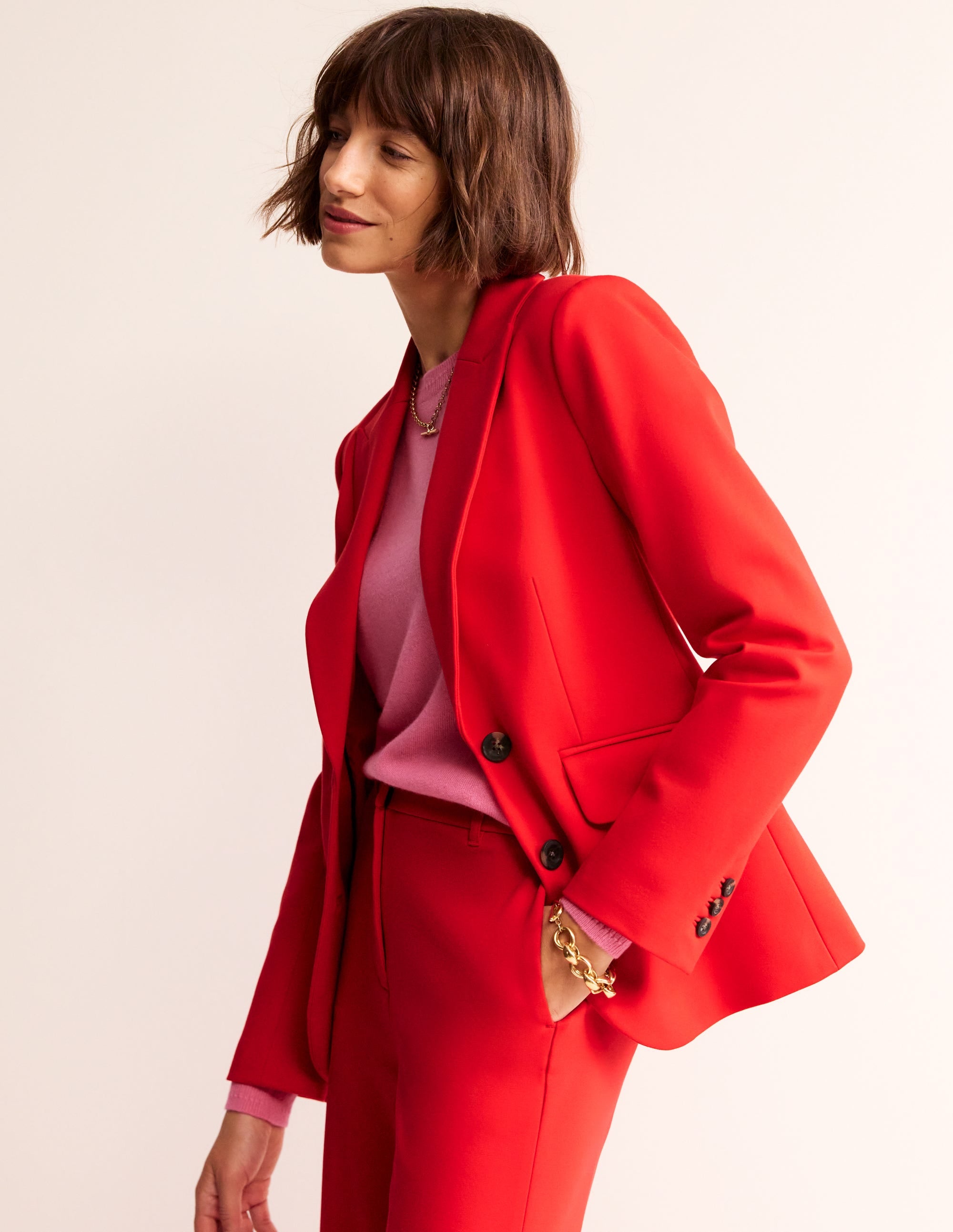 A woman wearing a bright red blazer with a pink top underneath, standing against a plain background.