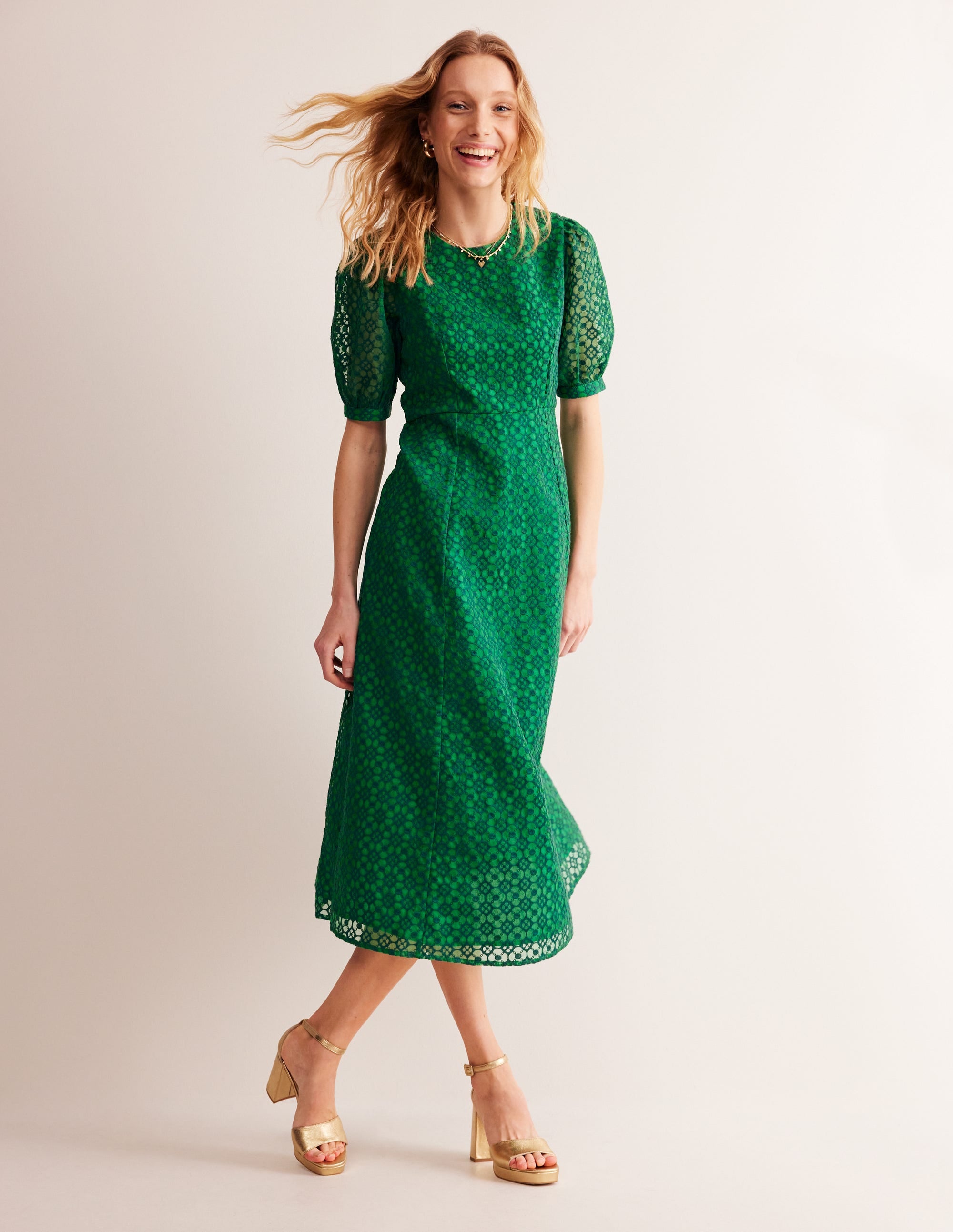 A woman wearing a green patterned organza dress with sheer puff sleeves, fitted waist, and a flared skirt that reaches the low calf.