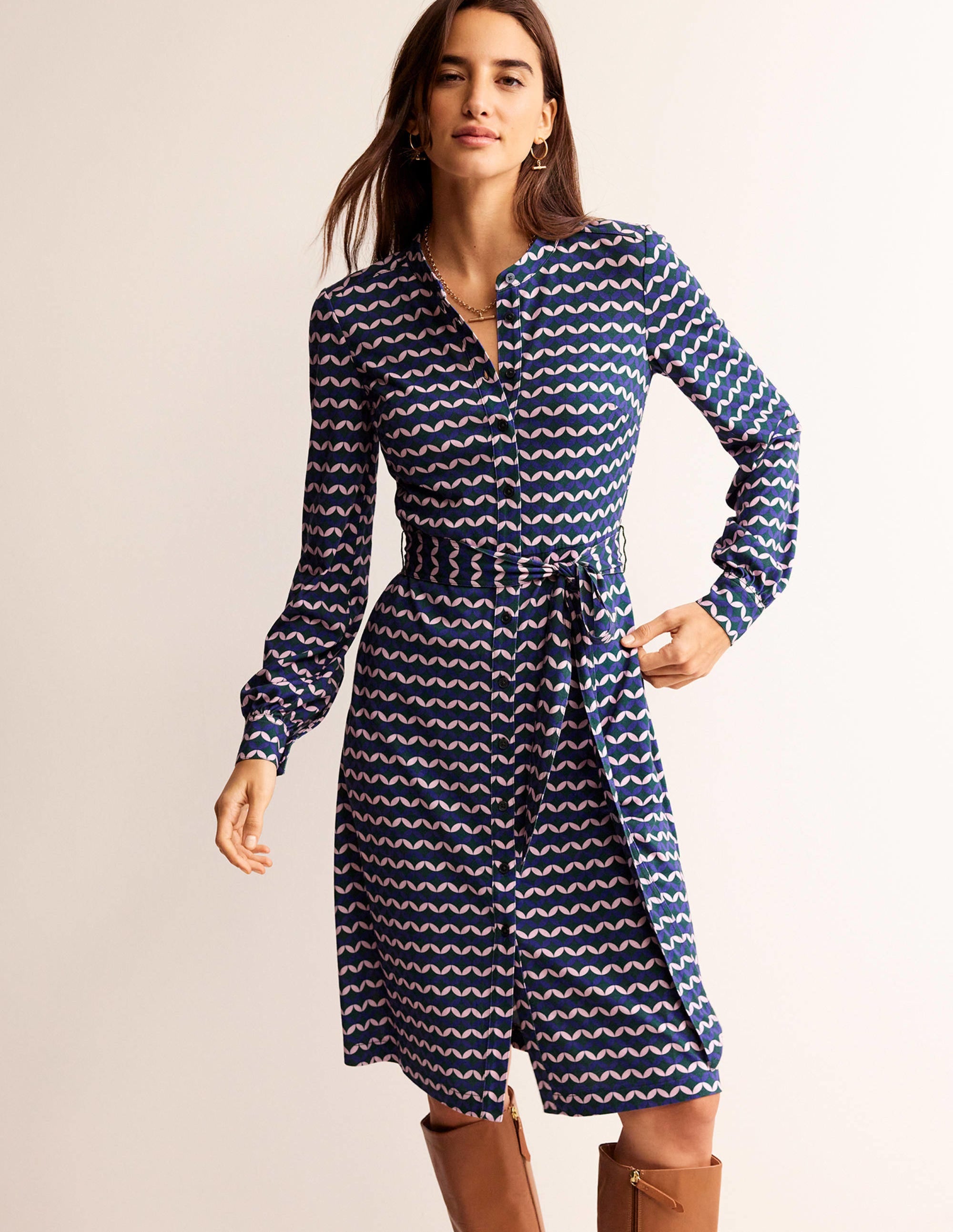 A woman wearing a navy shirt dress with pink and white geometric pattern, long sleeves with cuffs, and a waist tie.