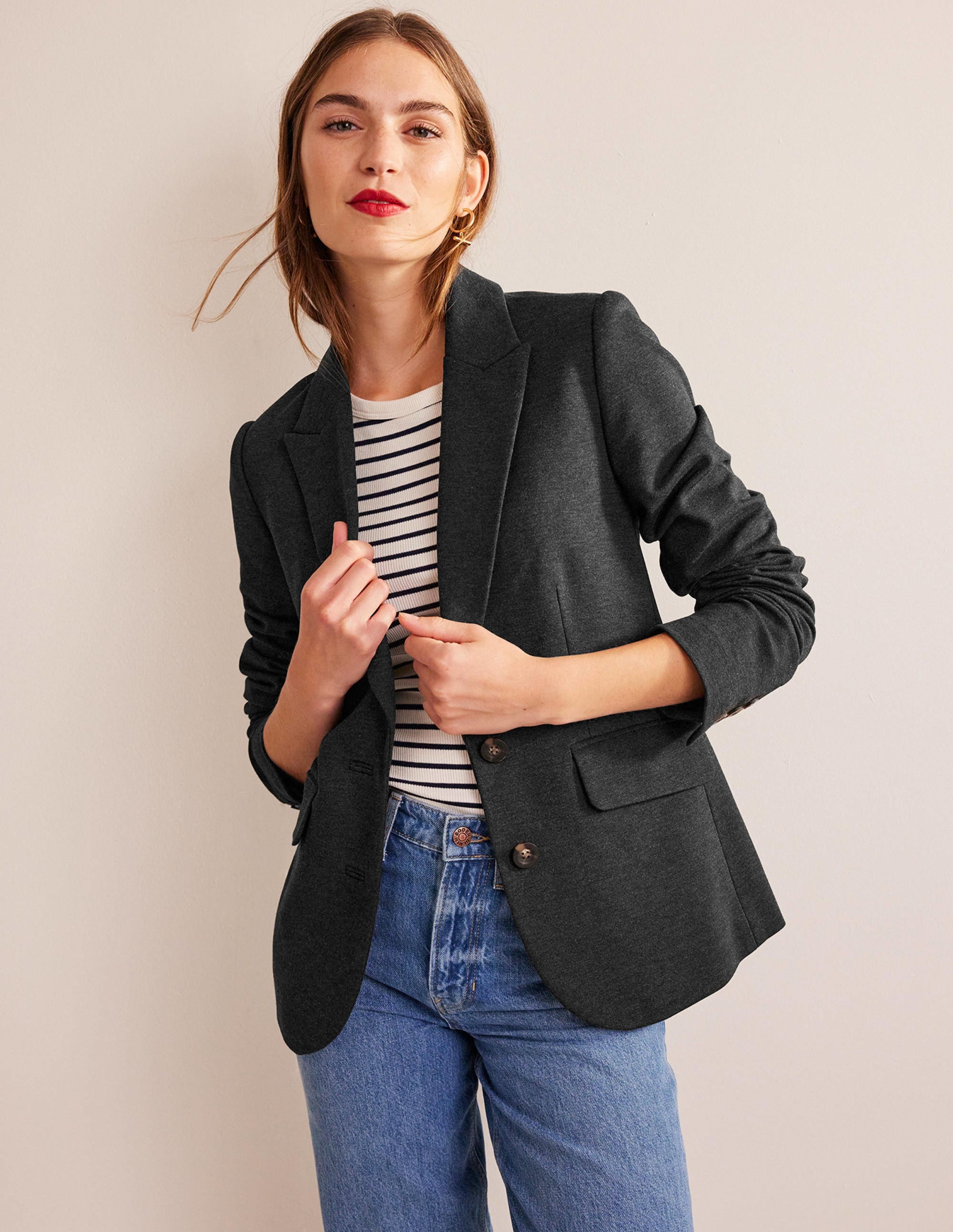 A woman wearing a charcoal marl blazer with a button front, notched lapels, and functional pockets, paired with a striped top and blue jeans.