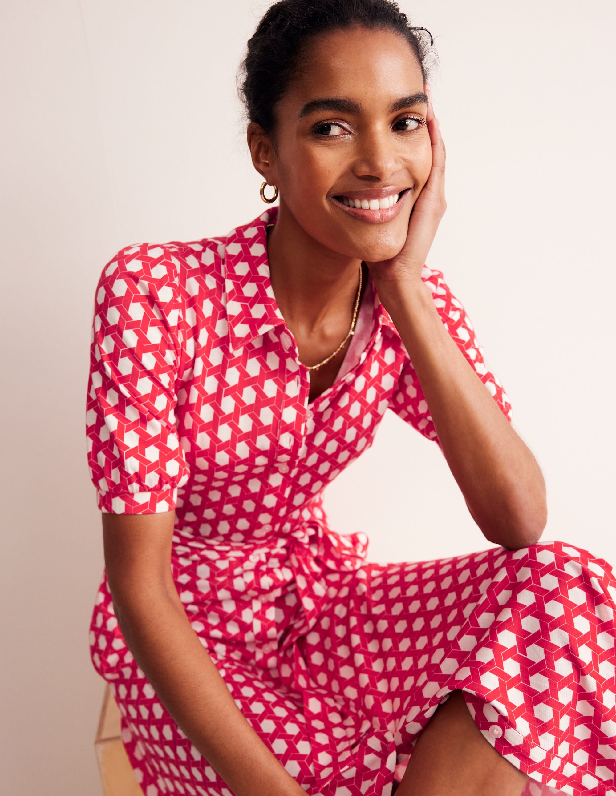 A woman wearing a Flame Scarlet midi shirt dress with a honeycomb geometric pattern, featuring puffed sleeves, a waist belt, and a button-up front.