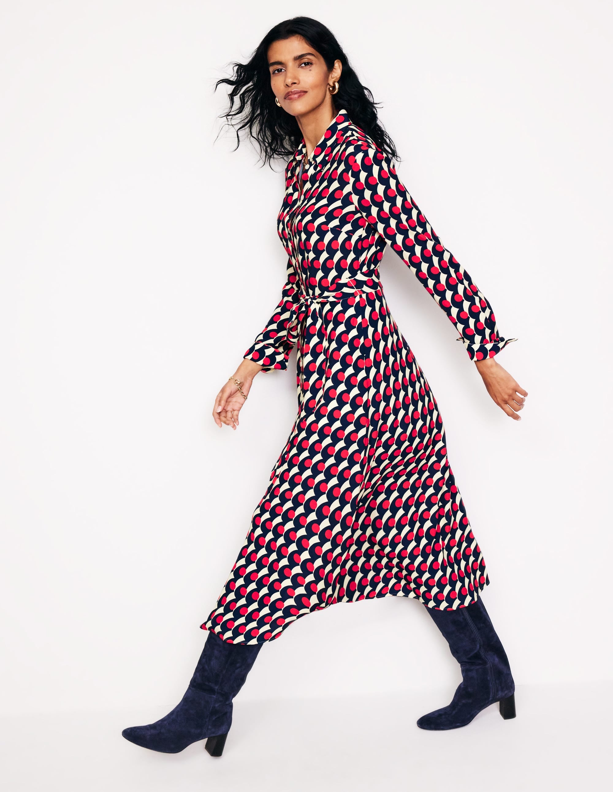 A woman wearing a red midi shirt dress with a polka wave pattern, pointed collar, waist belt, and full-length sleeves, paired with navy boots.