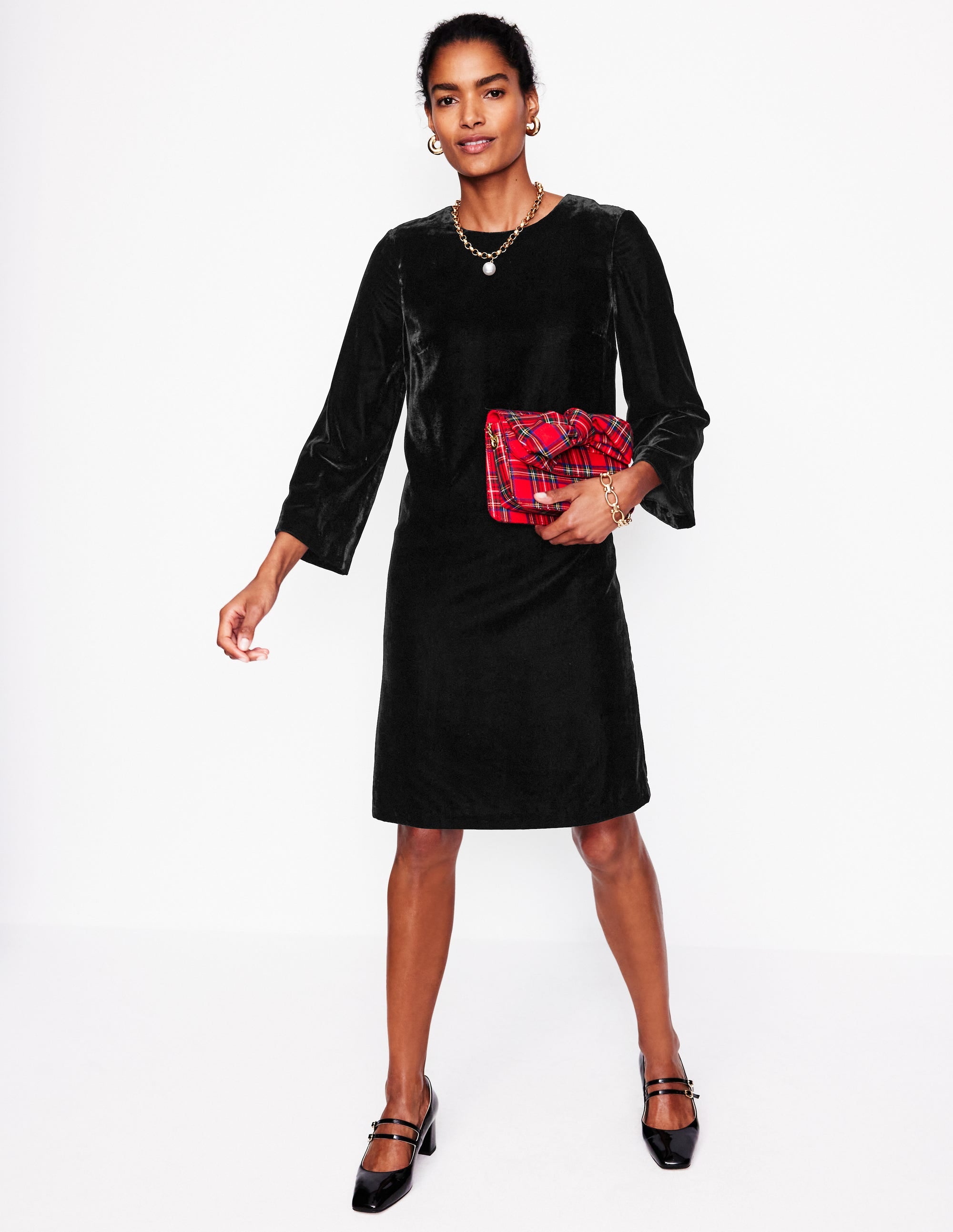 A woman wearing a black velvet long-sleeve shift dress with a straight fit, full lining, and a concealed back zipper.