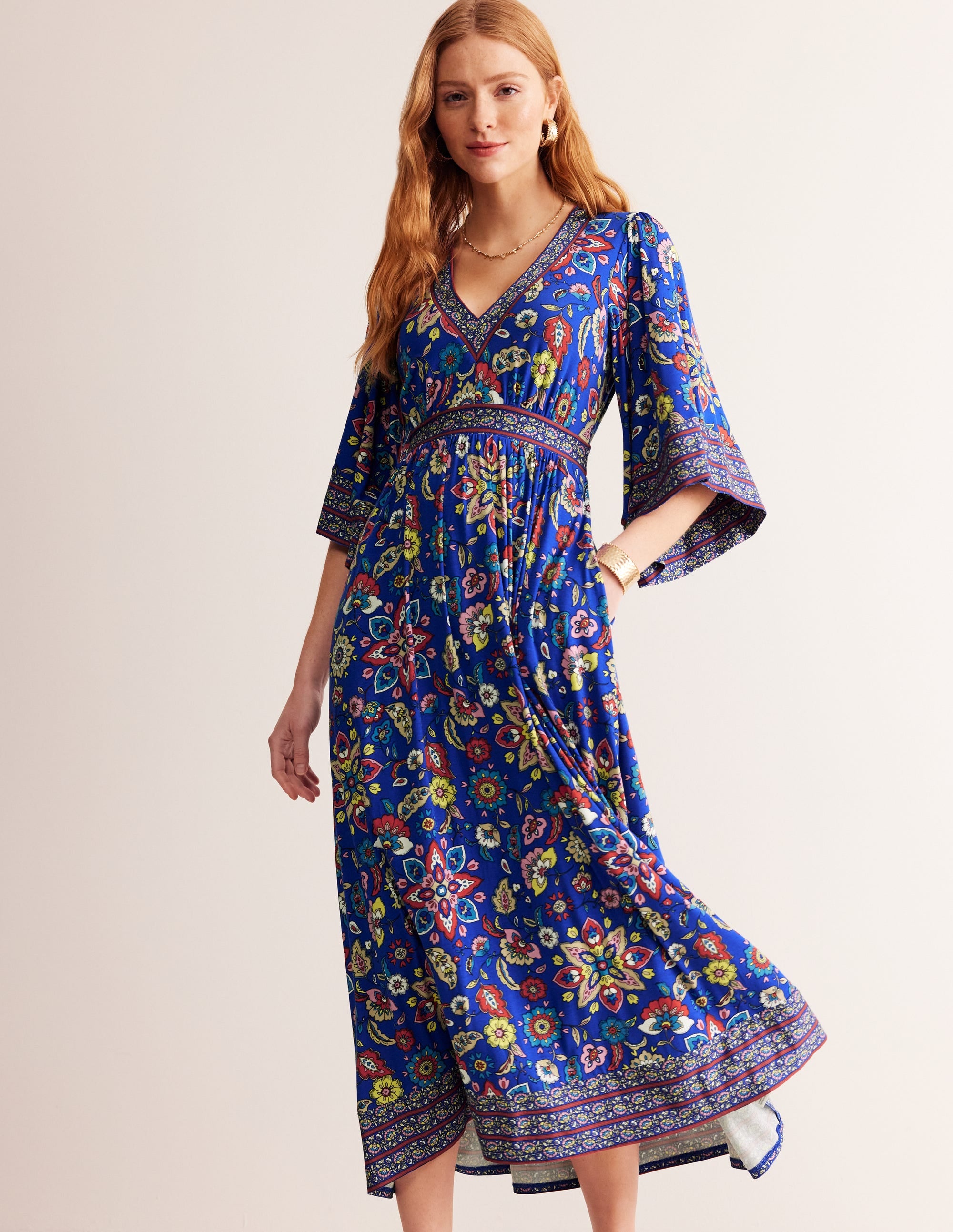 A woman wearing a blue maxi dress with a colorful botanical print, kimono sleeves, and a deep V-neck.