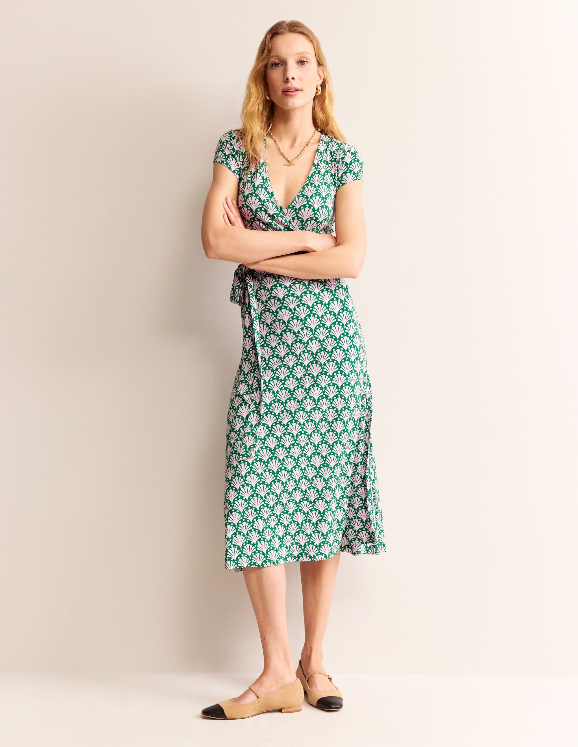 A woman wearing a sweet lilac midi wrap dress with a shell pattern, V-neckline, cap sleeves, and a slim fit.