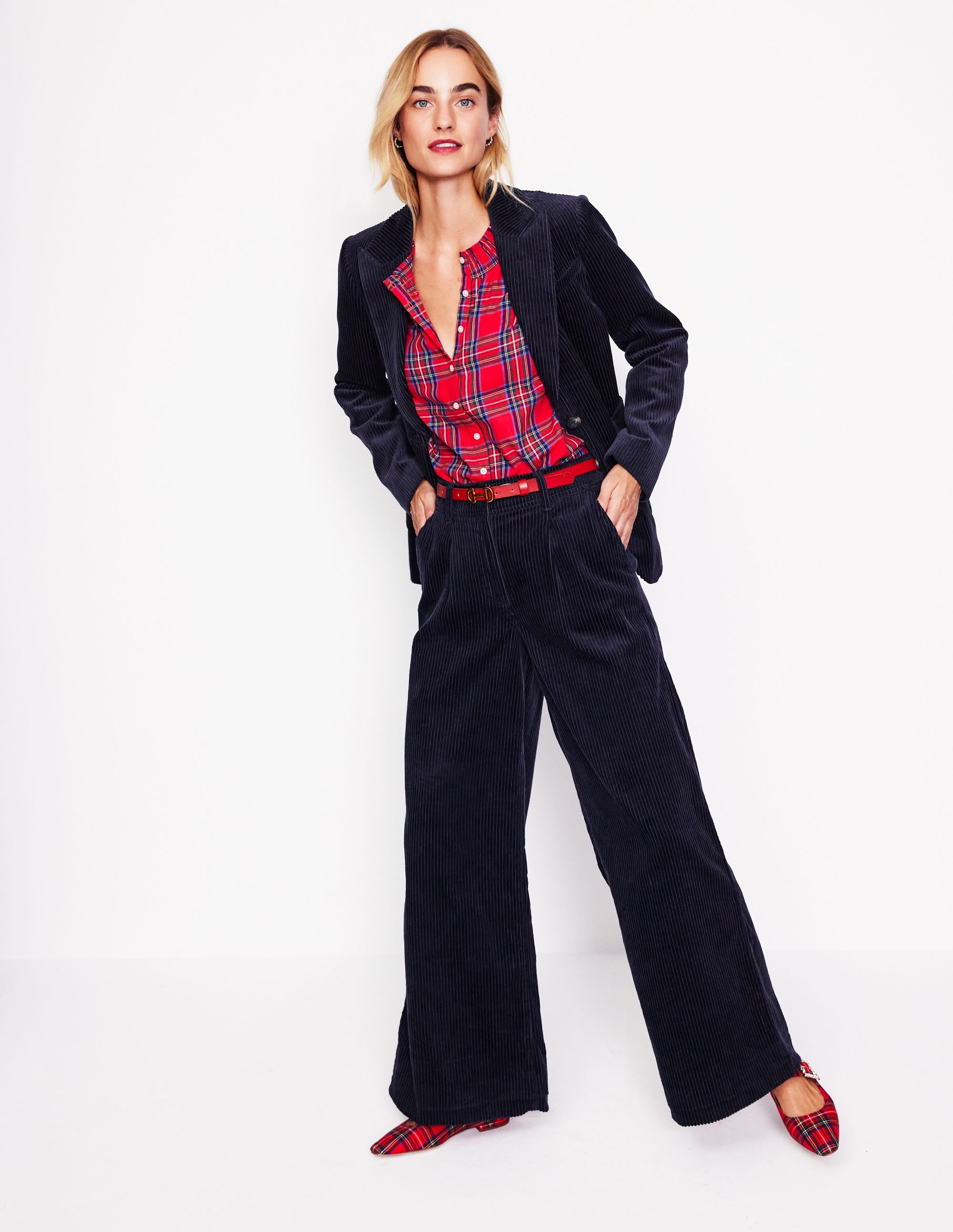 A woman wearing navy corduroy trousers with wide legs, a red plaid shirt, a navy blazer, and red plaid shoes.