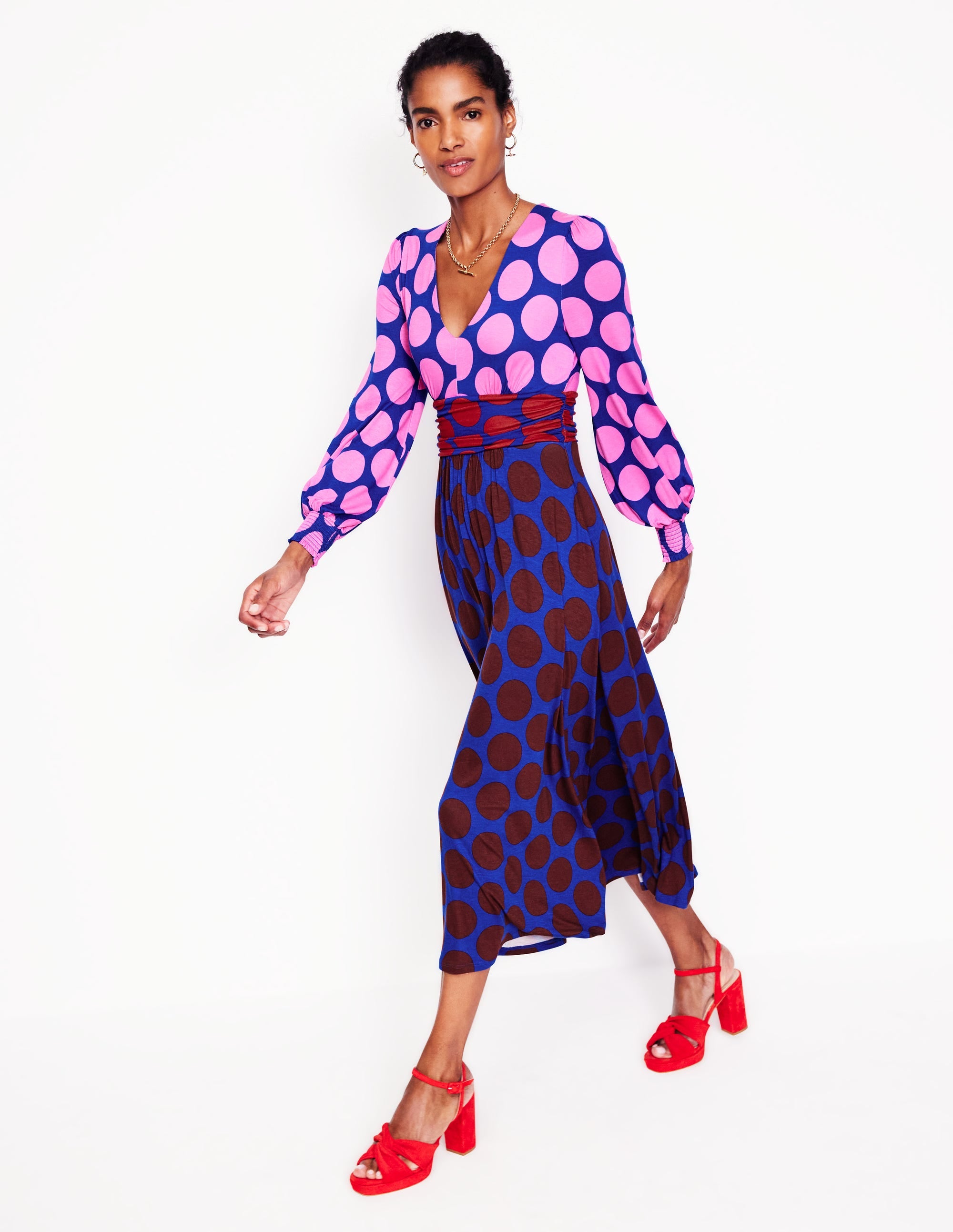 A woman wearing a pink maxi dress with large pink spots, ruched waist, and blouson sleeves.