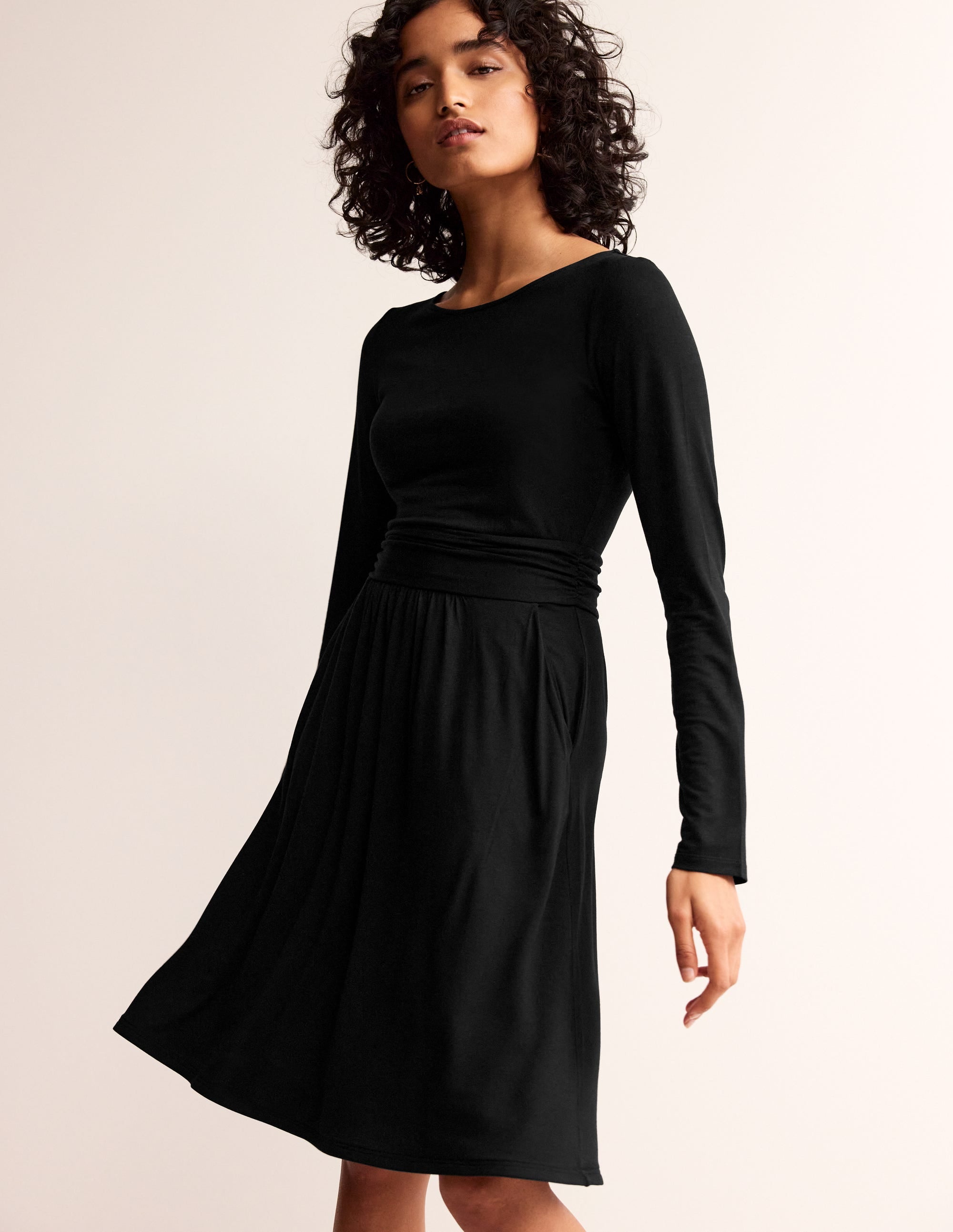 A woman wearing a black long sleeve dress with a fitted waist and pockets, made from soft jersey fabric.