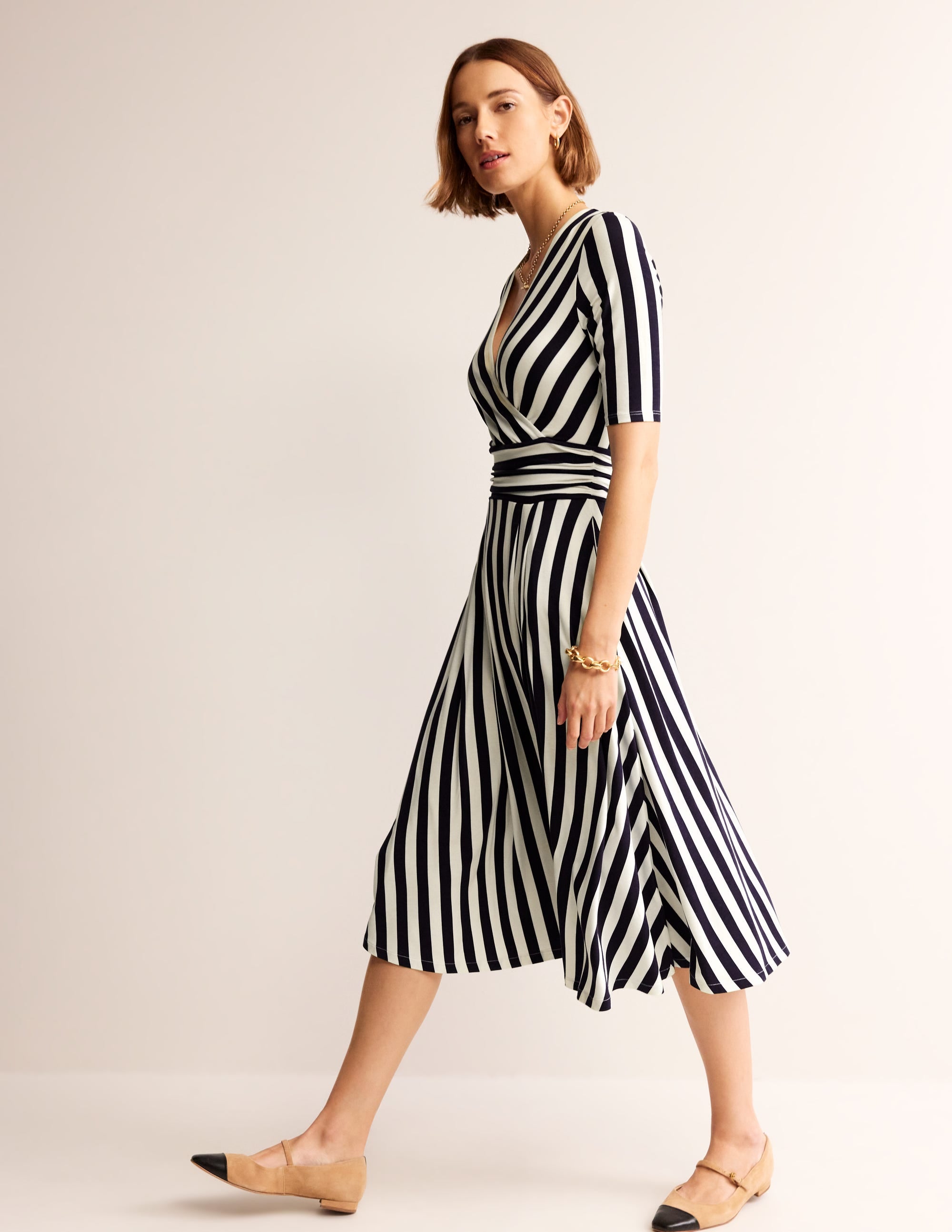 A woman wearing a striped midi dress with a V-neck, ballet sleeves, and side pockets, in navy and ivory colors.