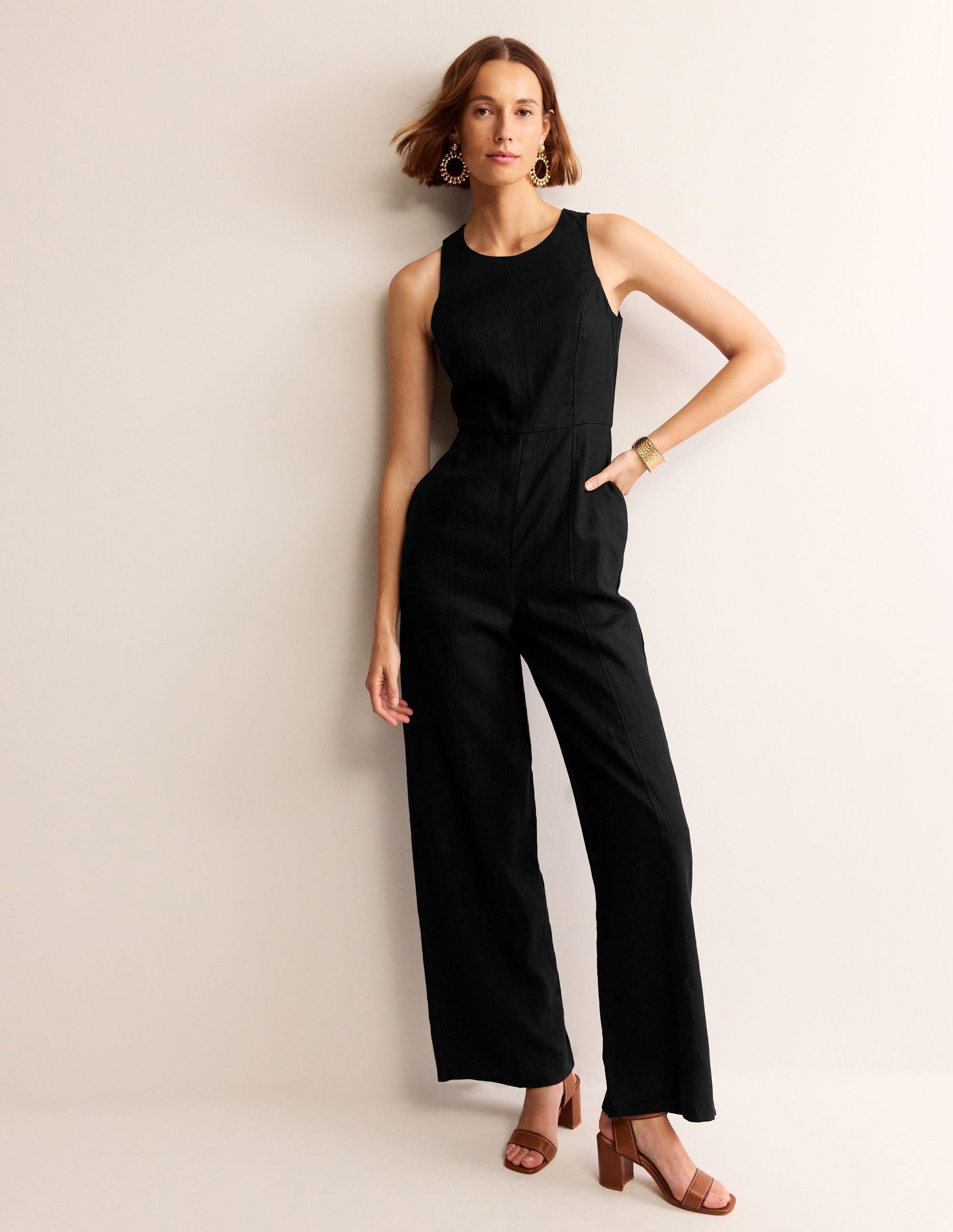 A woman wearing a sleeveless black linen jumpsuit with side pockets, a back zip, and a keyhole at the back.