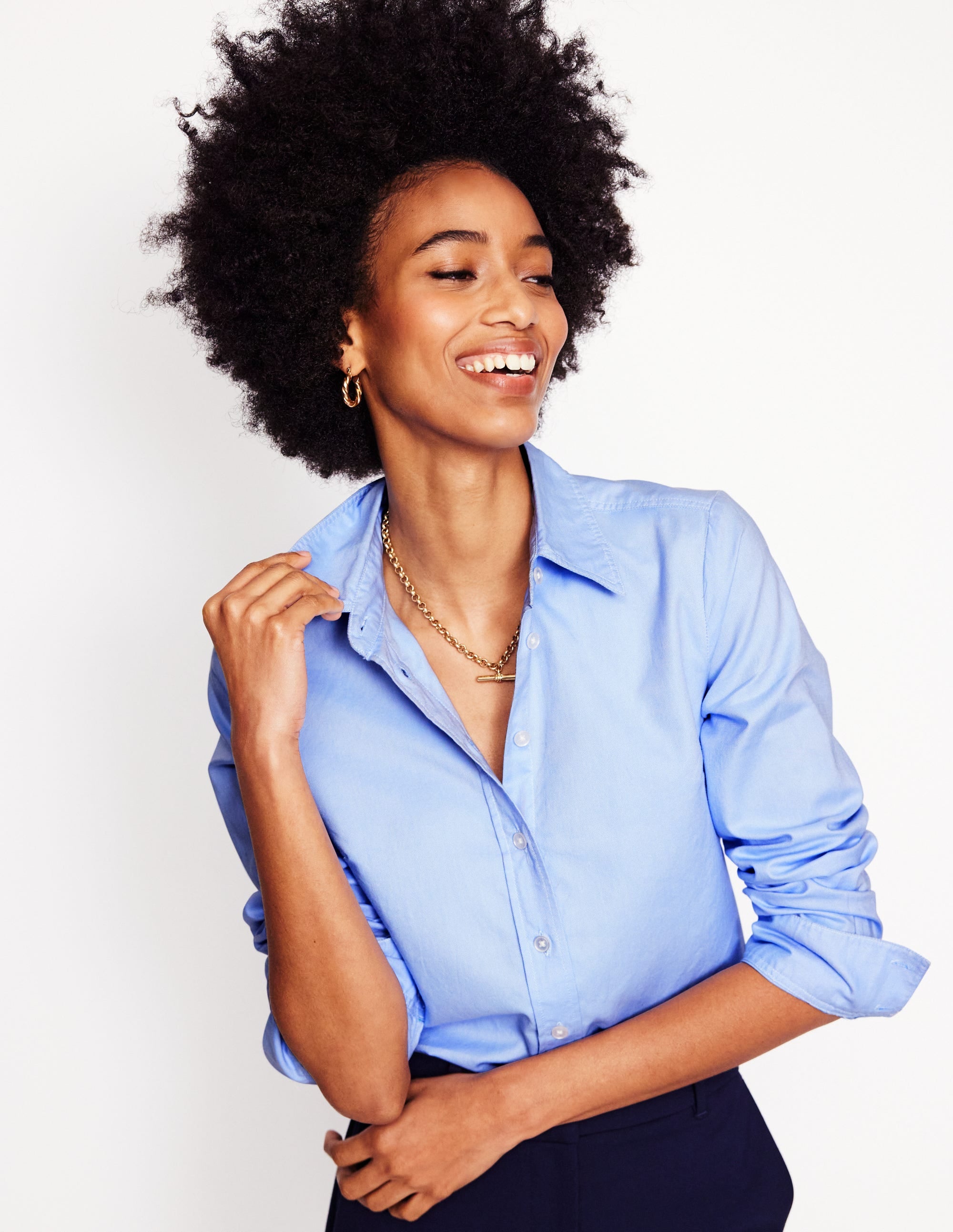 A woman wearing a blue Oxford cotton shirt with a curved hem, long sleeves, and a classic collar.
