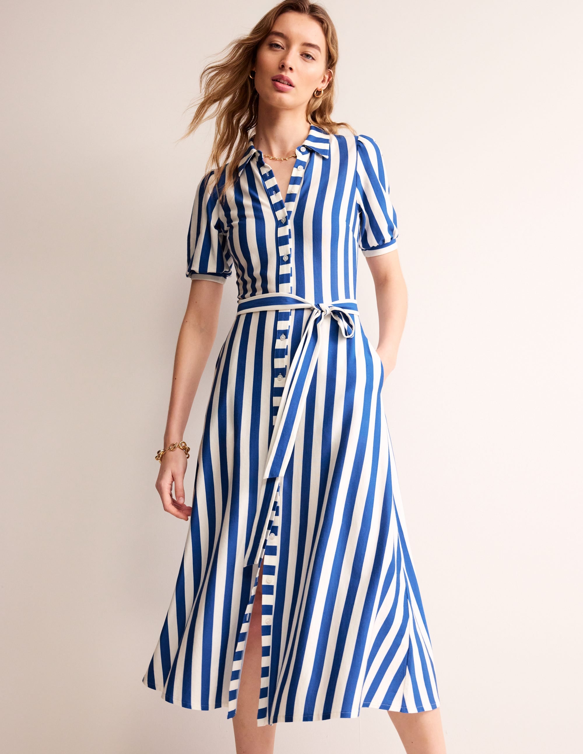 A woman wearing a blue and ivory striped midi shirt dress with puffed sleeves and a waist belt.