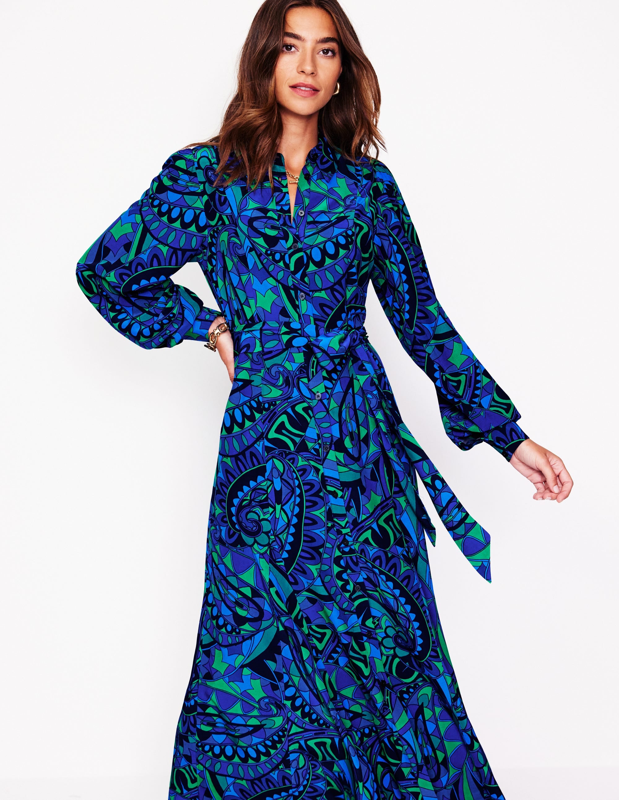 A woman wearing a blue maxi shirt dress with a kaleidoscopic paisley pattern, long sleeves, and a waist belt.