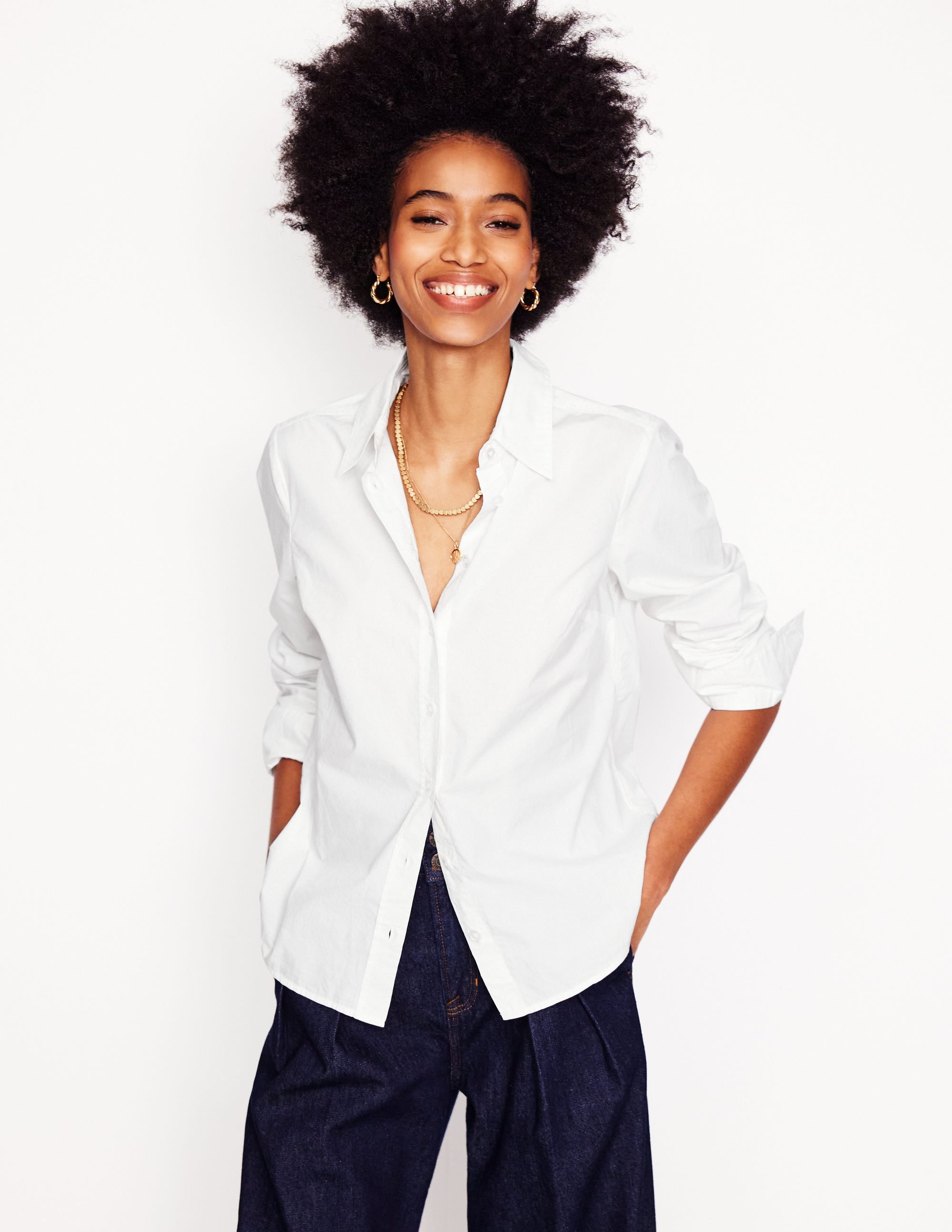 A woman wearing a white cotton shirt with long sleeves, a classic collar, and a curved hem at the back.
