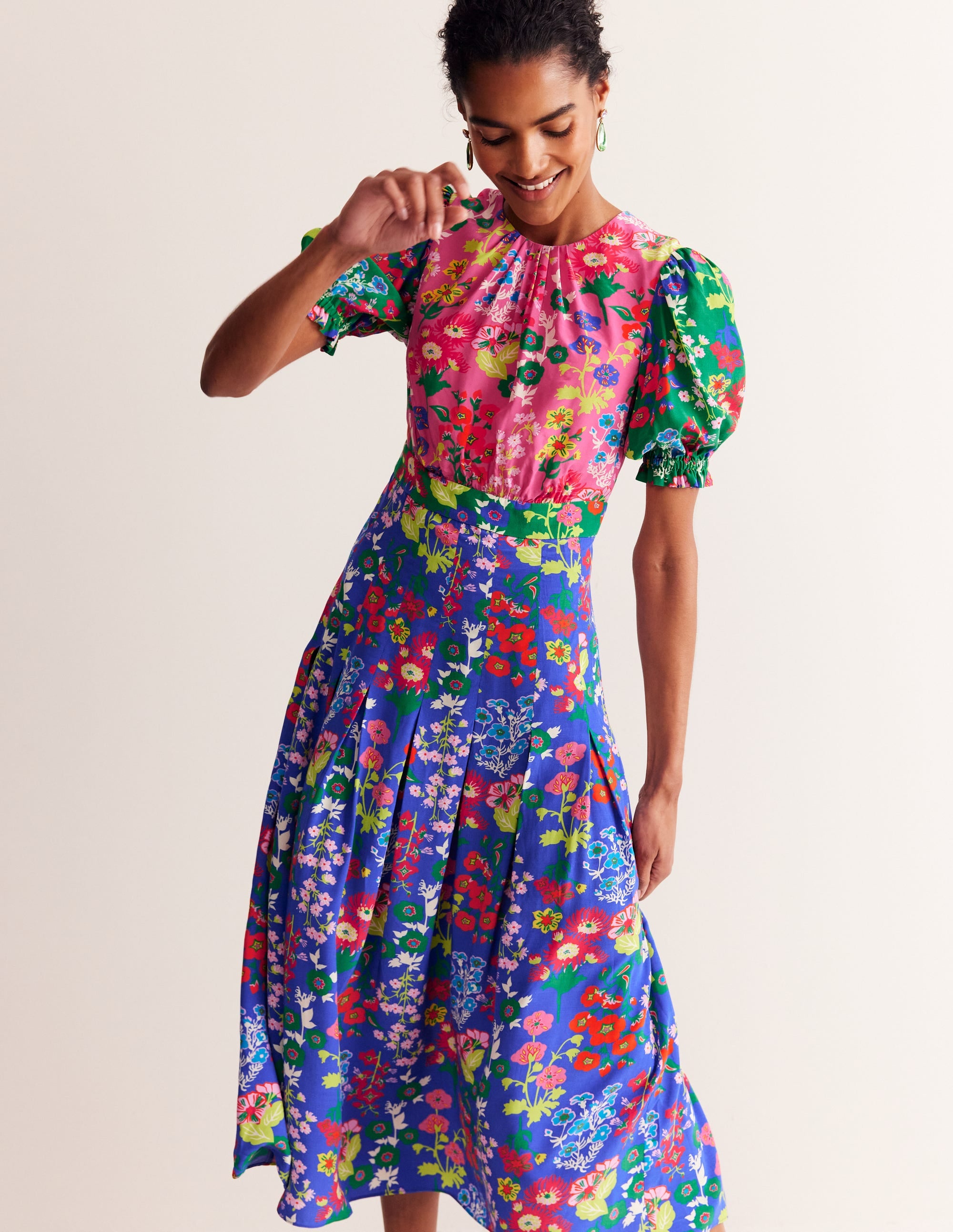 A woman wearing a colorful midi dress with a floral print, short smocked sleeves, and a gathered skirt.