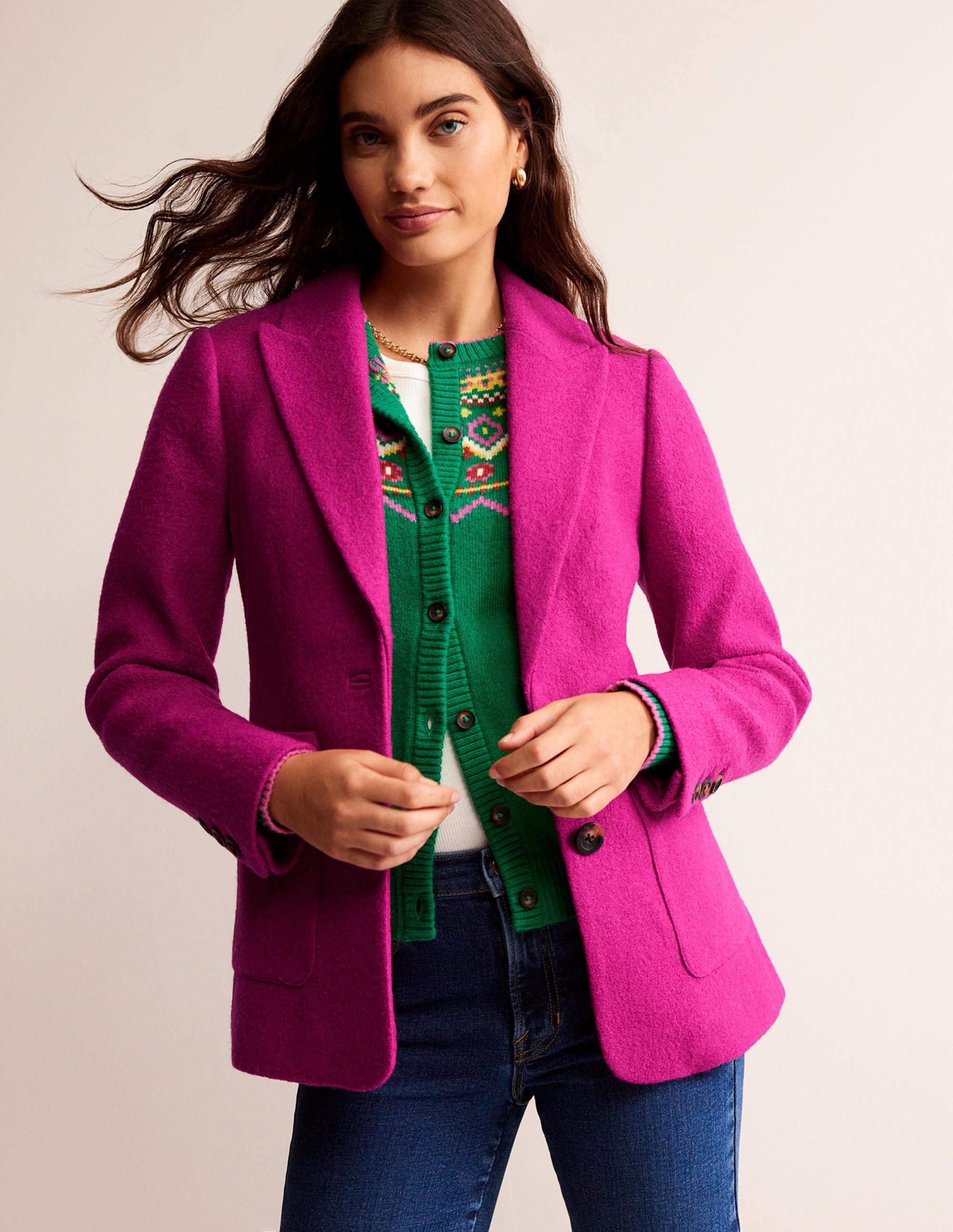 A woman wearing a magenta textured blazer with a revere collar, full-length sleeves, contrast piping, and welt pockets.