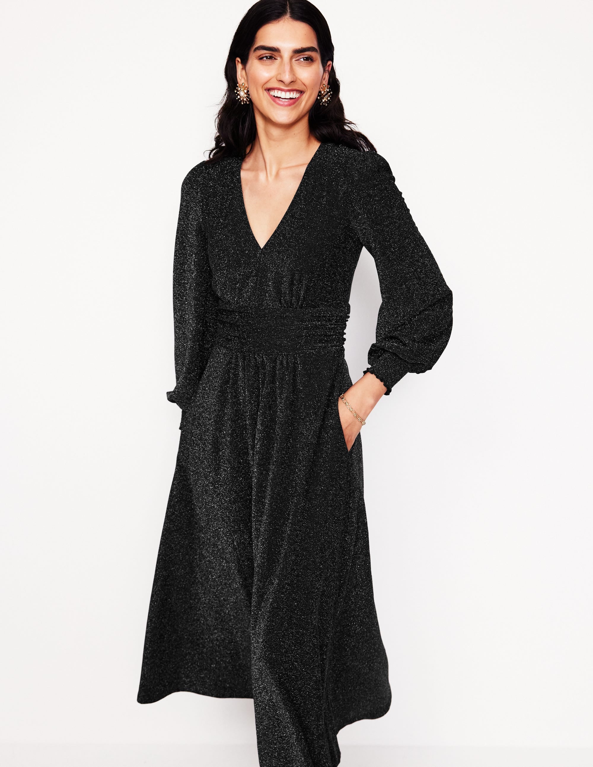 A woman wearing a black metallic midi dress with a V-neckline and long sleeves, standing against a plain background.