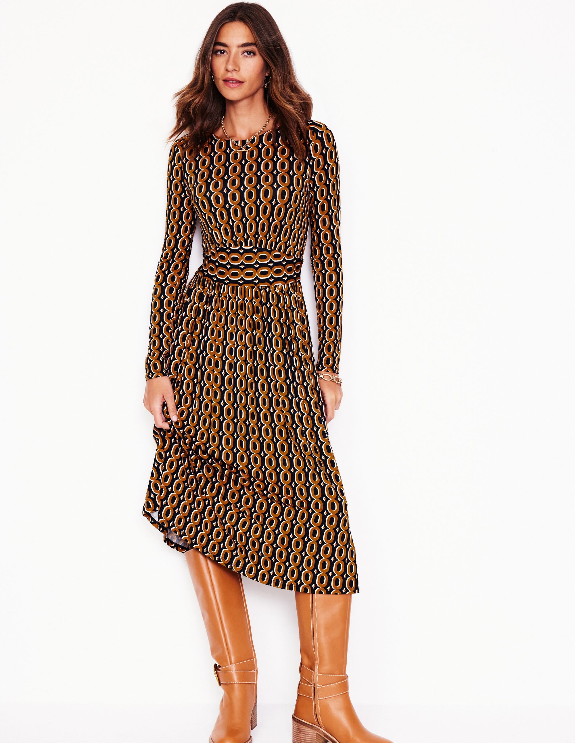 A woman wearing a long-sleeve jersey dress with a chain pattern in ochre, featuring a relaxed fit and side pockets.