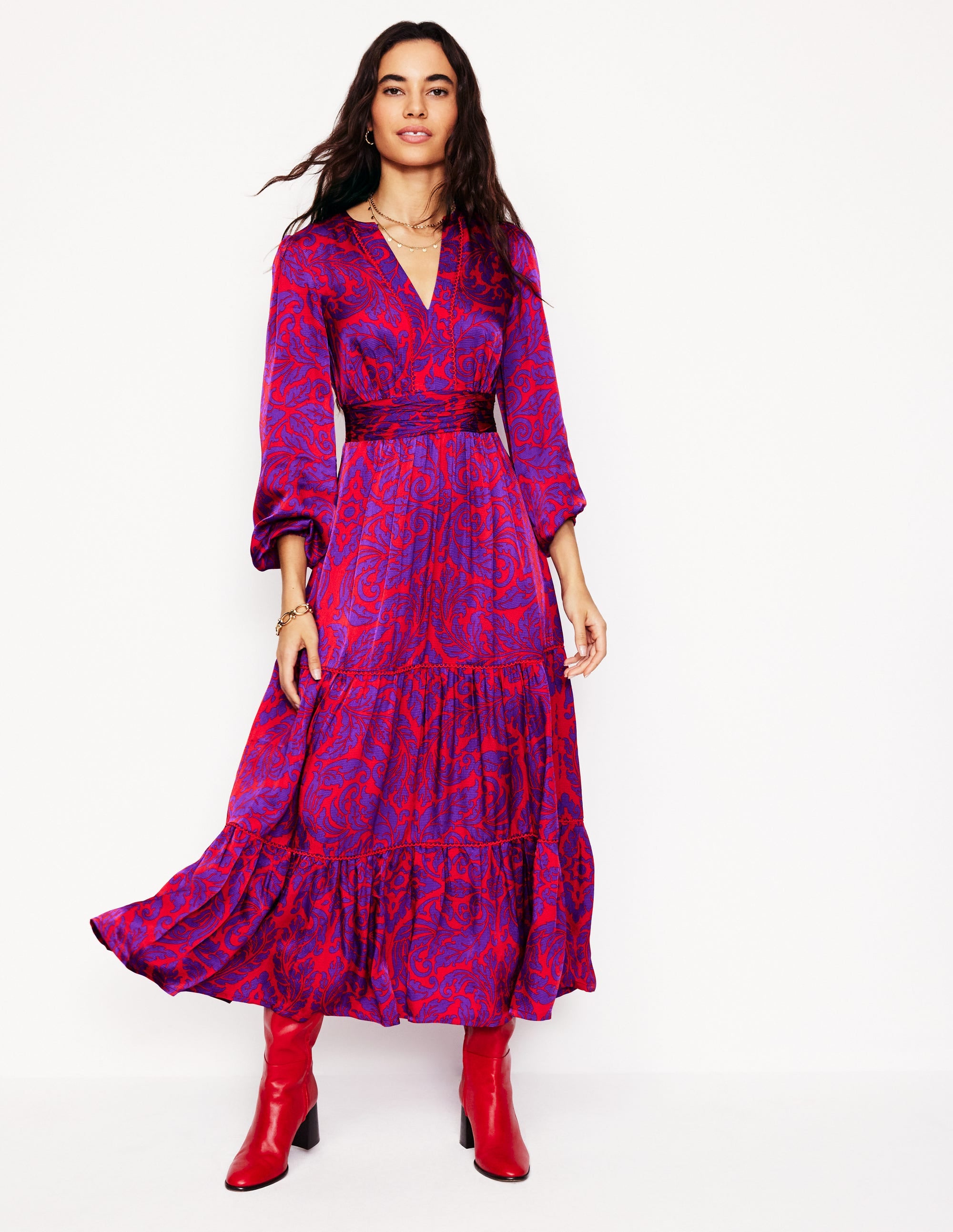 A woman wearing a purple satin maxi dress with an elaborate leaf pattern, long sleeves, and a tiered skirt.