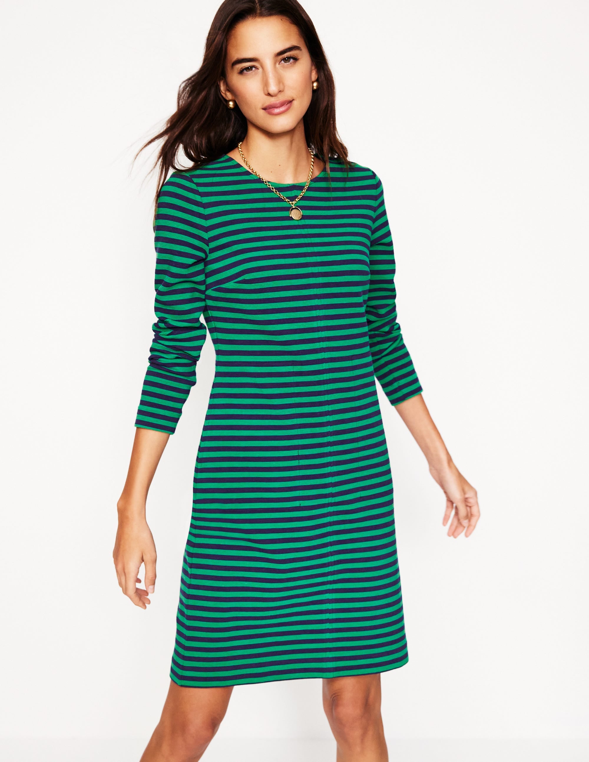 A woman wearing a knee-length dress with green and navy horizontal stripes, long sleeves, and a round neckline.