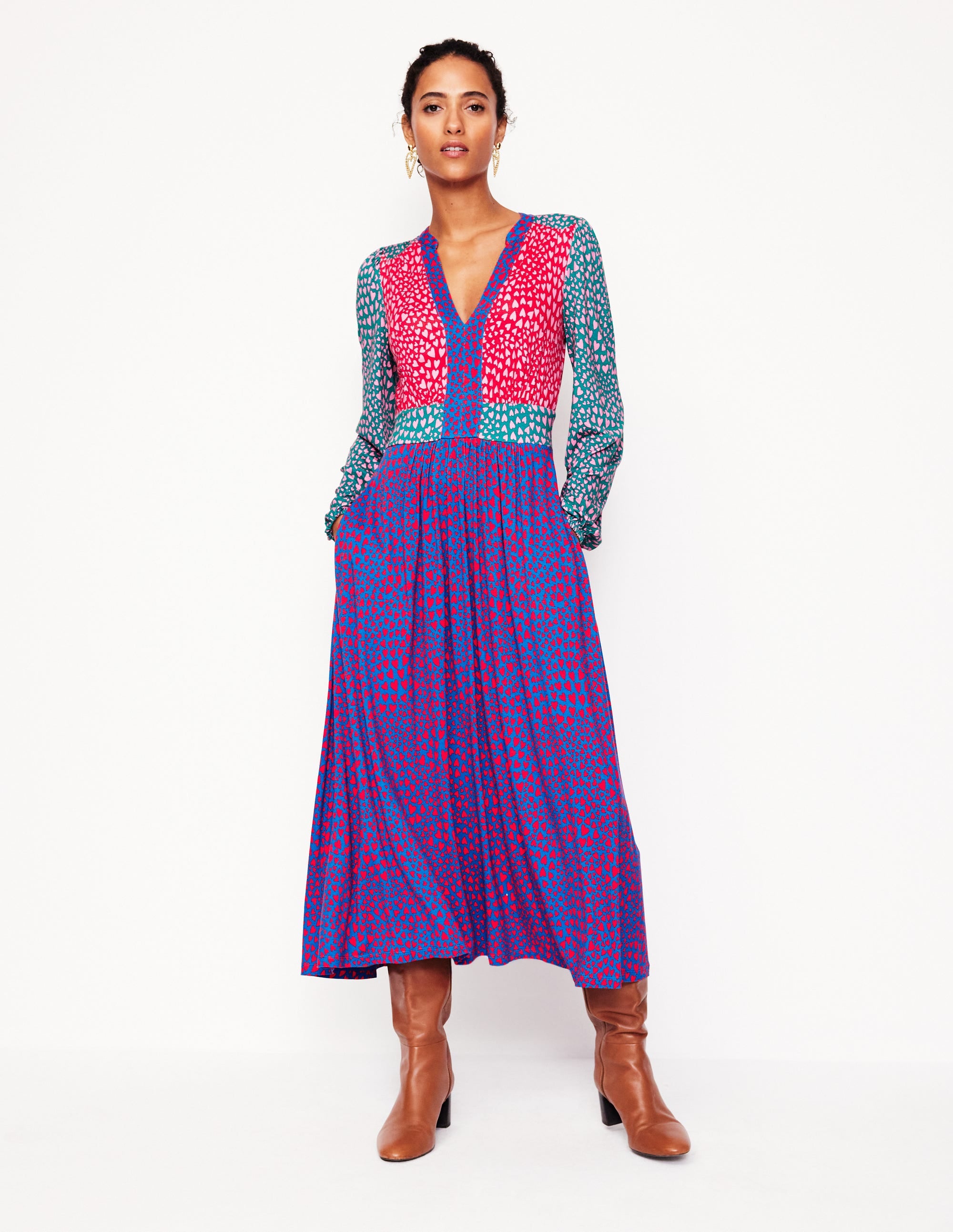 A woman wearing a multicolour long sleeve midi dress with a heart cluster pattern, puffed sleeves, and a V-neckline, paired with brown boots.